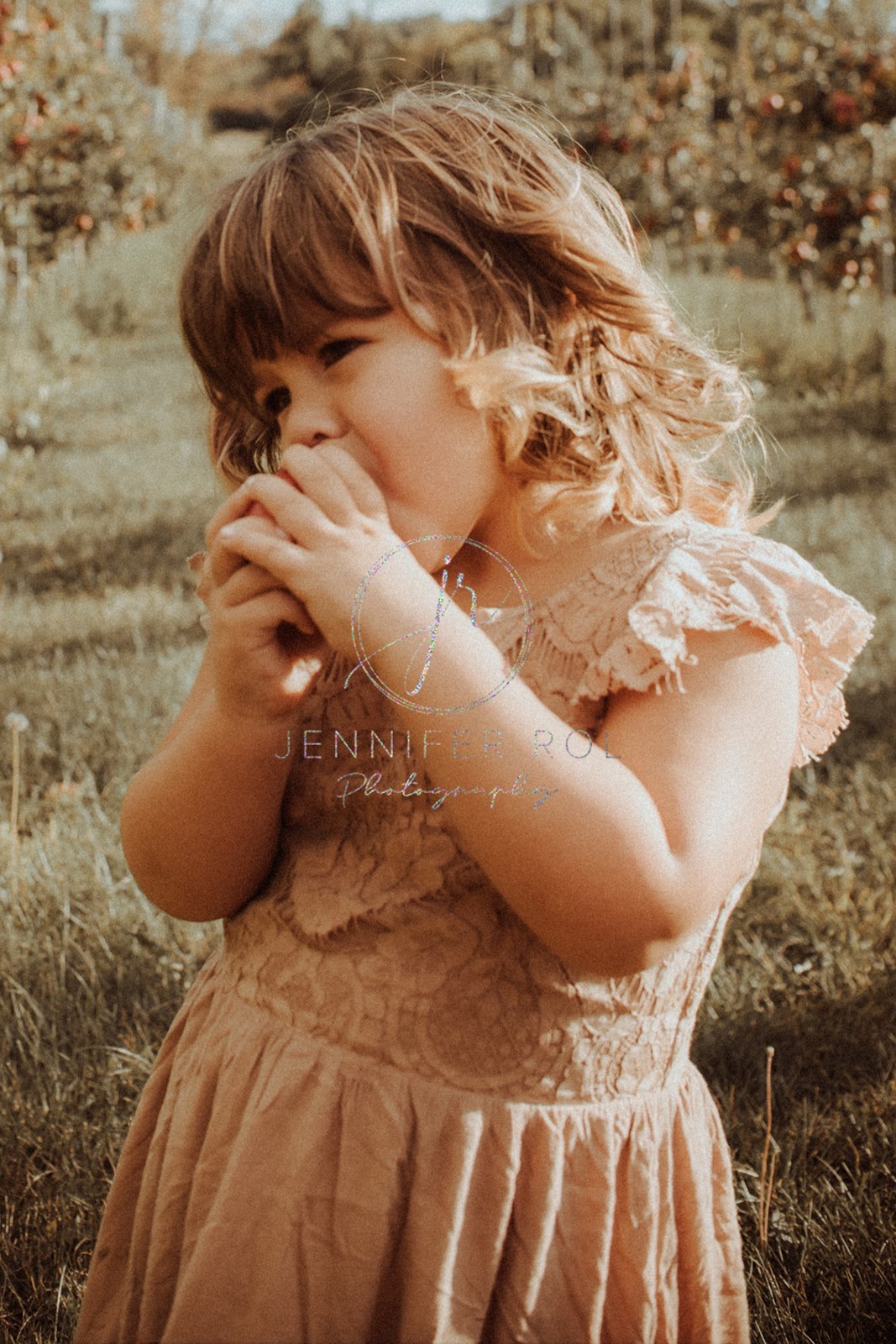 A young girl in a pink dress takes a bite from an apple in an orchard at sunset after visiting Daycares in Missoula