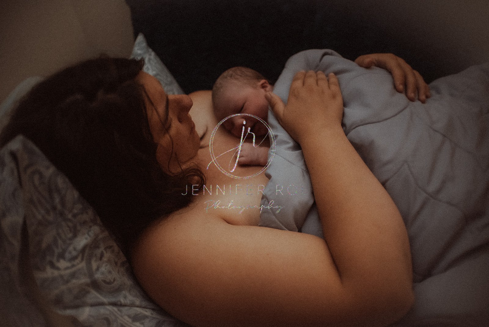 A mother lays on a couch with her newborn baby sleeping on her bare chest under a blanket