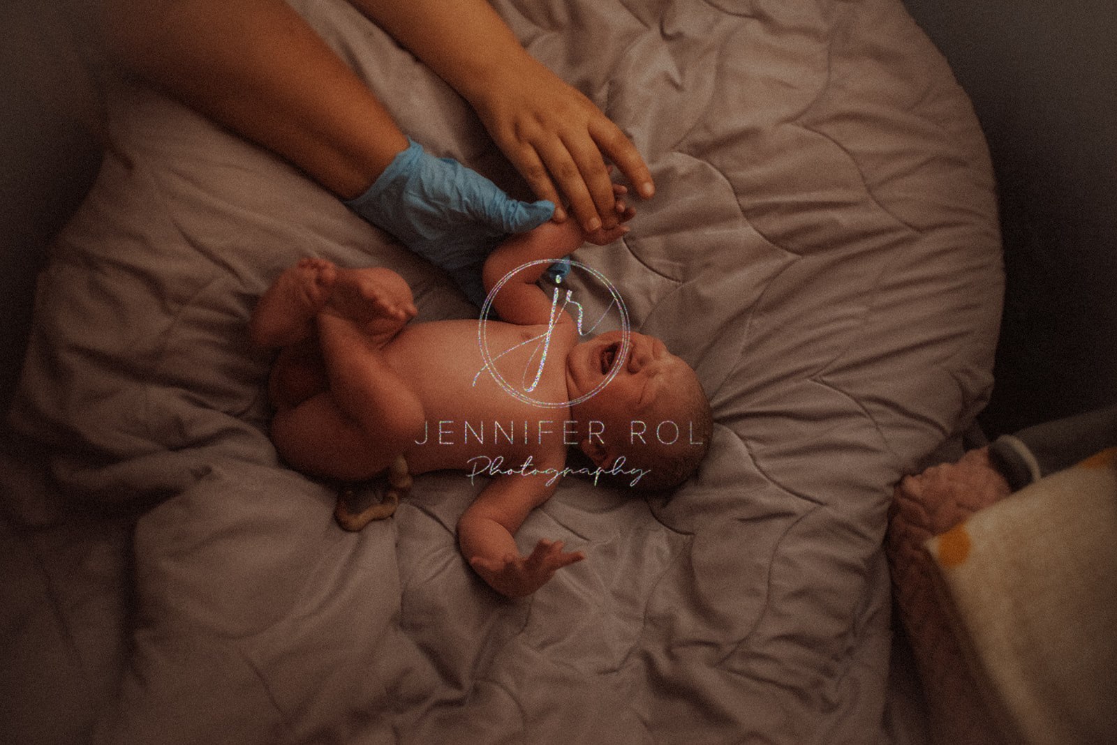 A newborn baby cries while laying on a blanket holding hands with mom and dad directly after birth with help from Doulas in Missoula