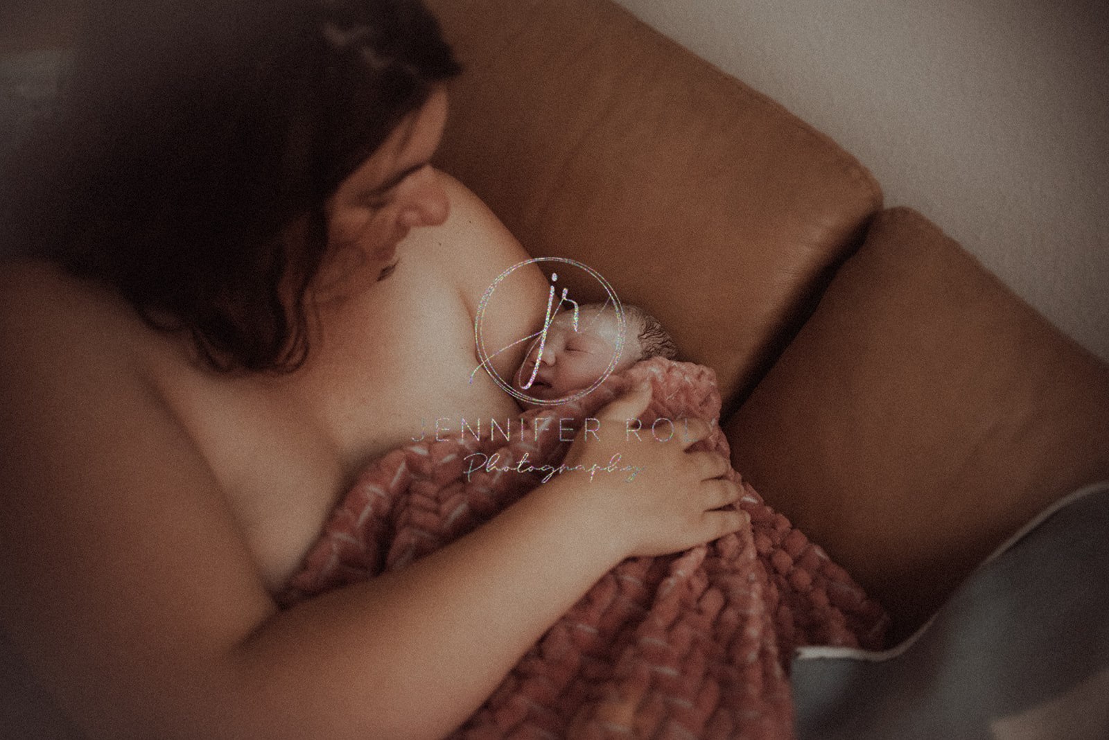 A mother cradles her freshly newborn baby on a leather couch after giving birth with help from Doulas in Missoula
