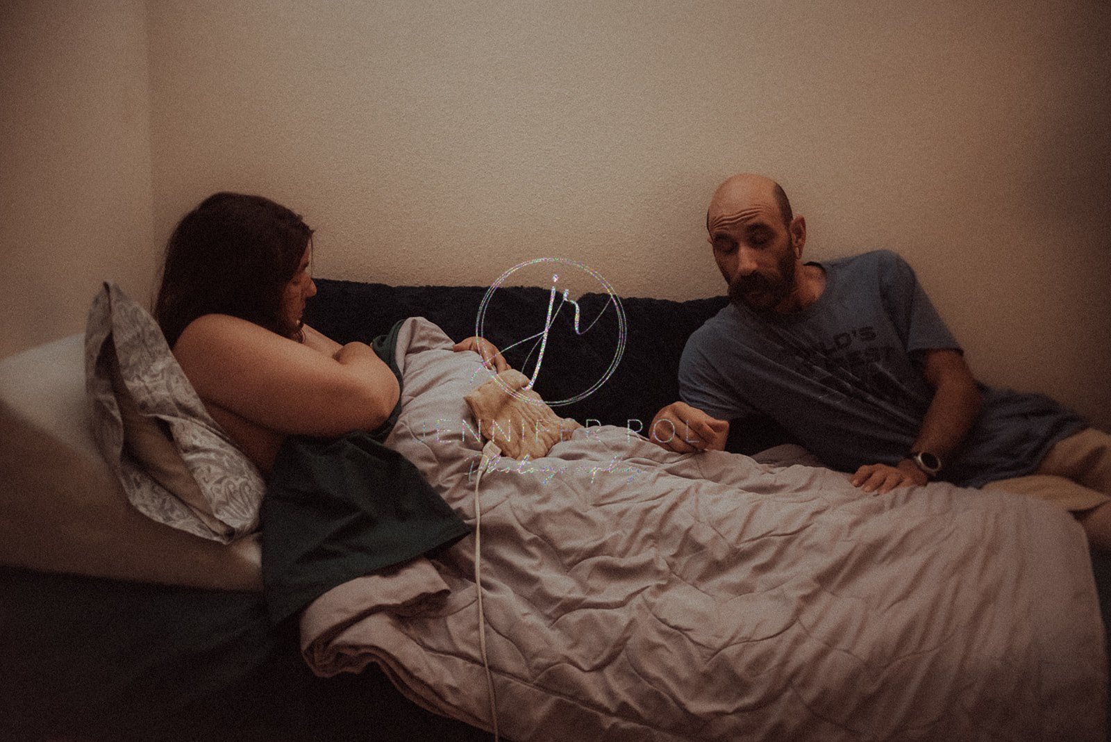 Happy new parents lay on a bed with their newborn baby directly after birth