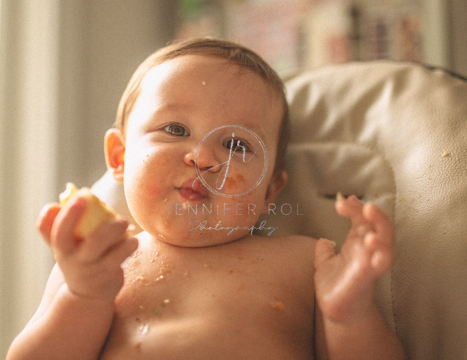 A happy toddler covered in food eats some fruit in a high chair