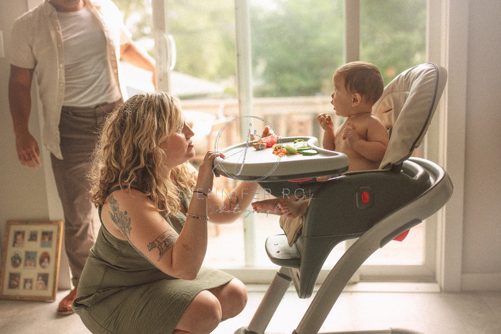 A mom kneels in front of her eating toddler in a high chair in the kitchen after visiting pediatric dentists in Missoula