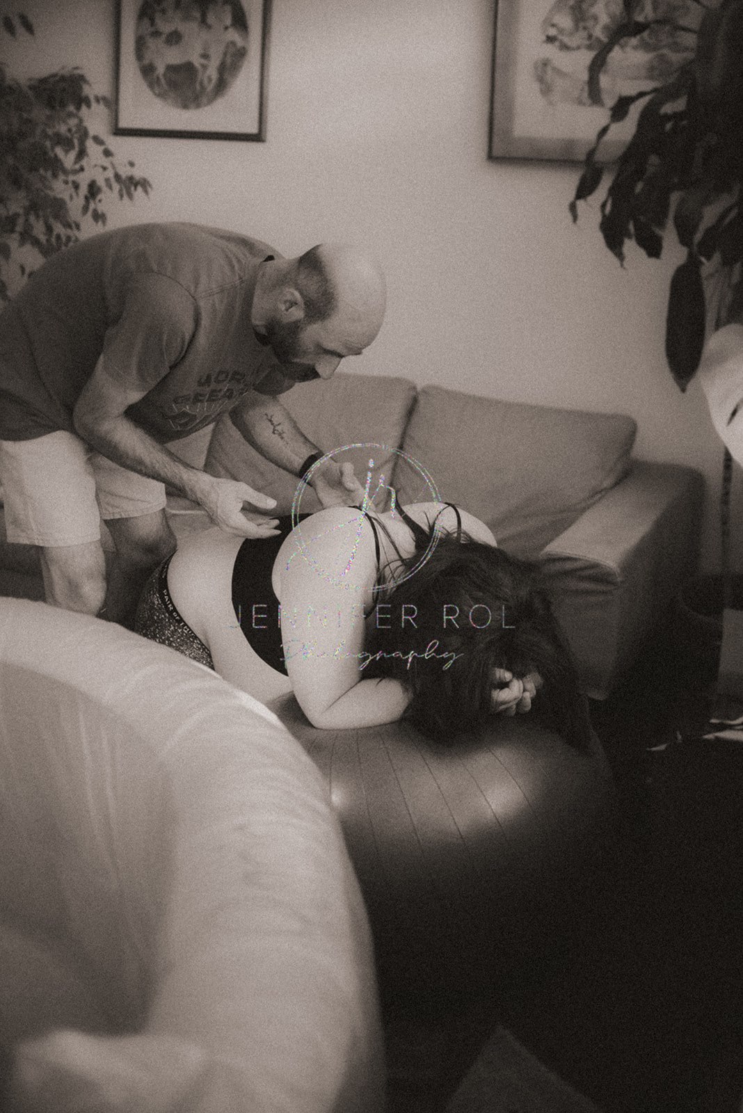 A mother in labor leans on a rubber workout ball with dad helping her