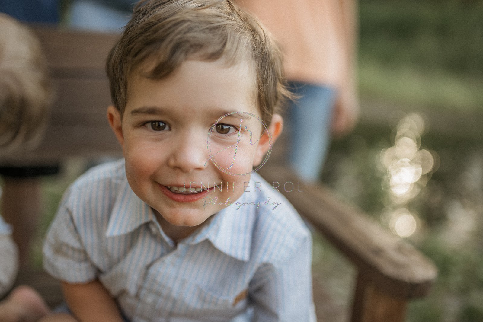 A happy toddler boy sits in a wooden bench smiling in a blue shirt