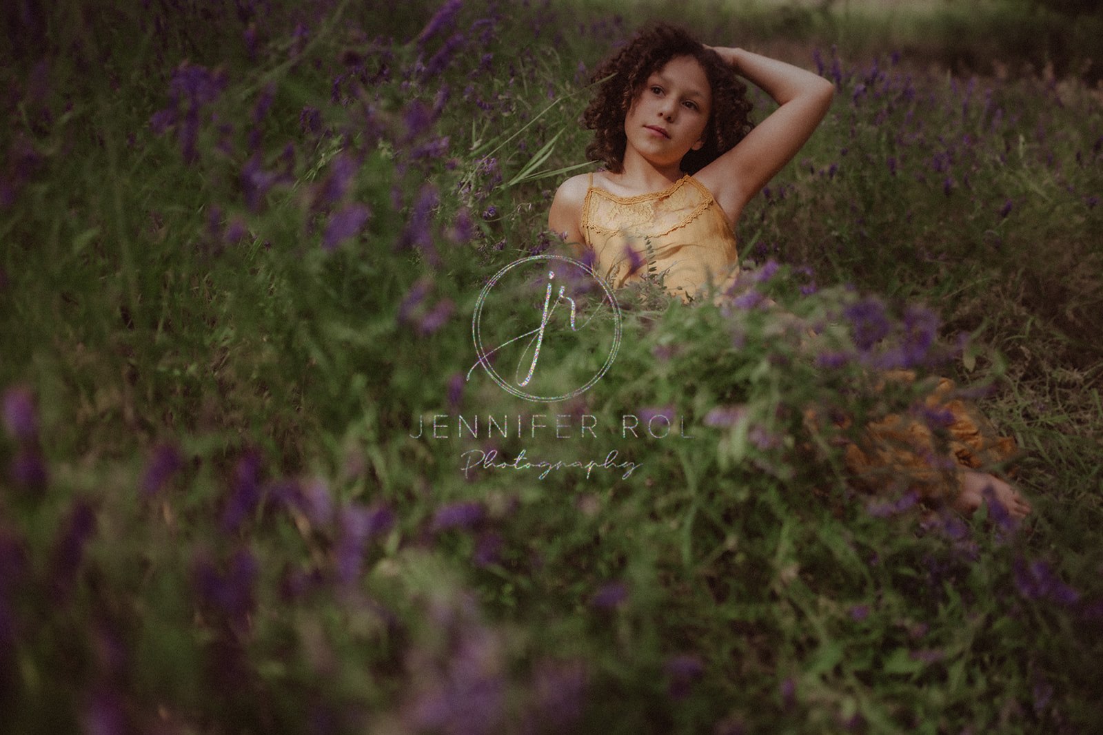 A young girl lounges in an orange dress in a field of wildflowers with a hand in her hair