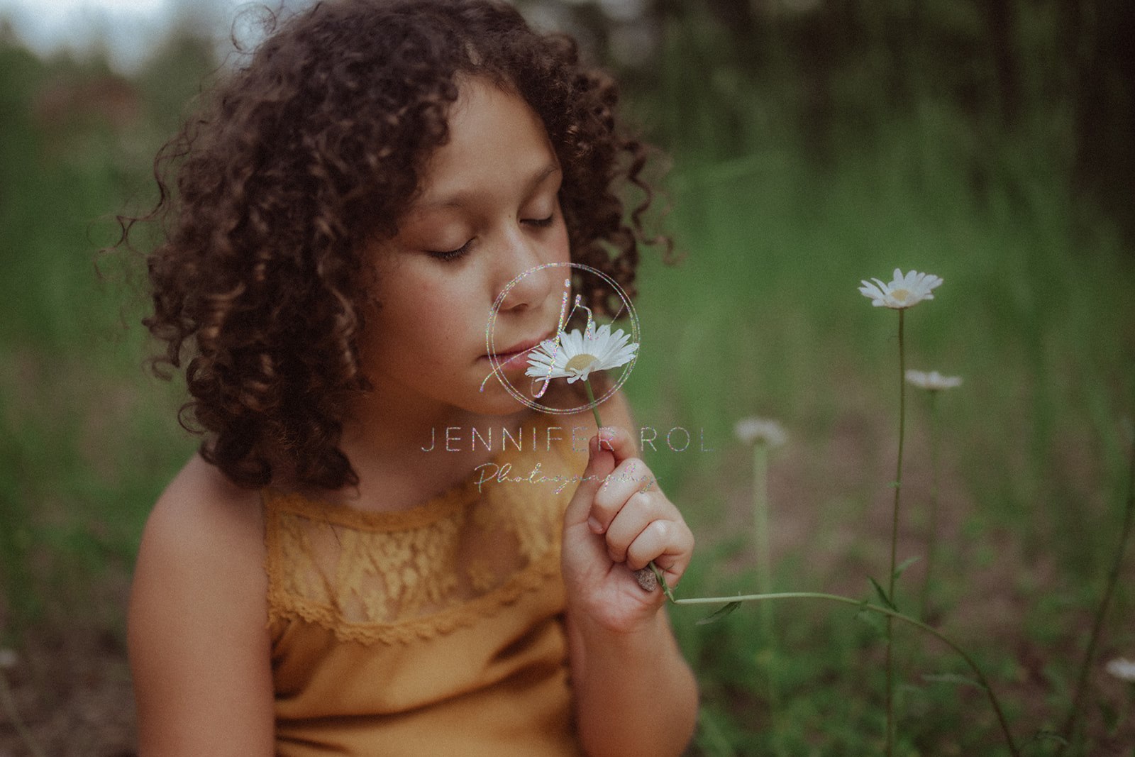 A young girl in an orange dress smells a wild daisy while sitting in a field before visiting Children's Museum in Missoula