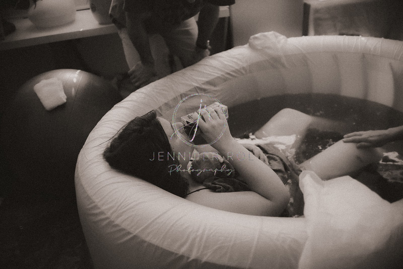 A mom just after labor drinks from a carton while in the birthing pool with her newborn baby after visiting chiropractors in Missoula