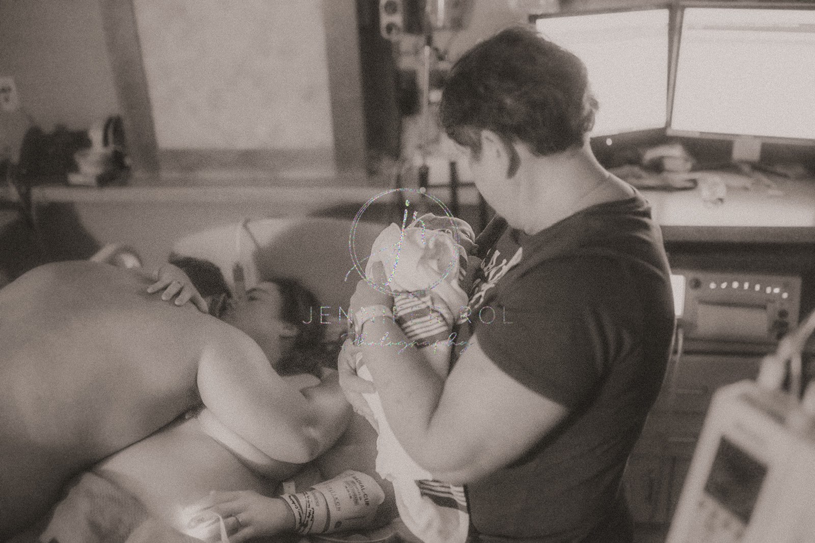 New parents embrace on the delivery room bed while a doula holds the baby before finding a diaper service in Missoula