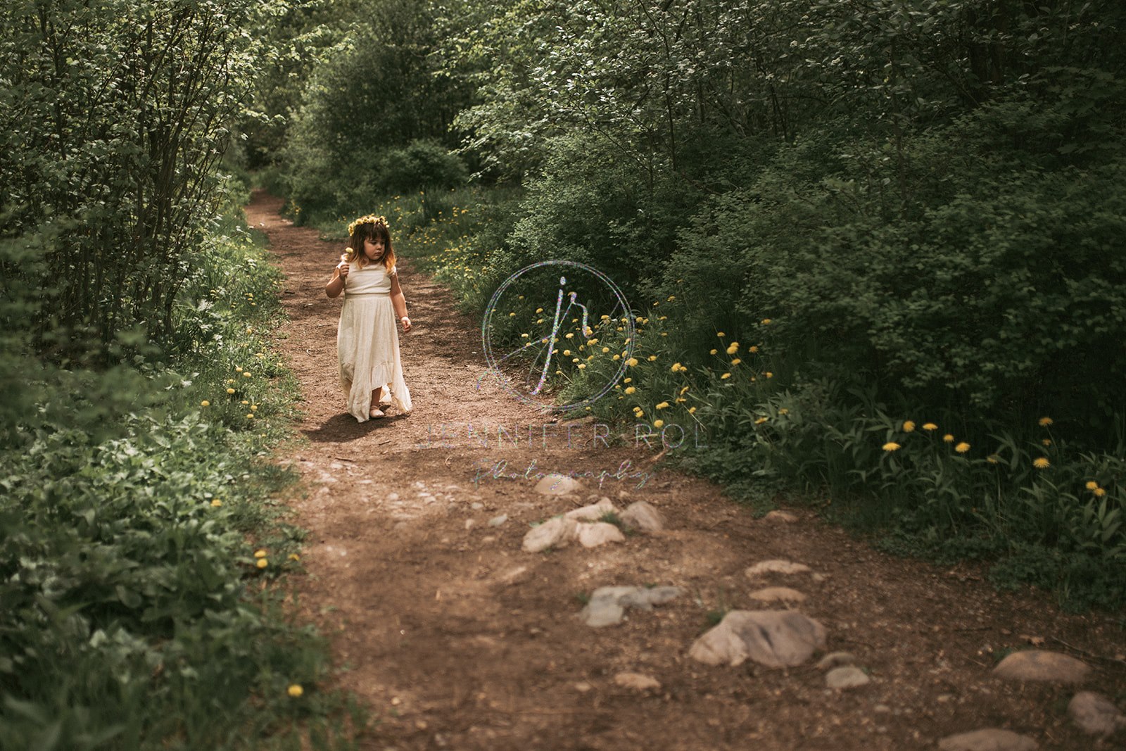 A toddler girl in a white dress walks on a park trail picking wildflowers after visiting Missoula birthday party places