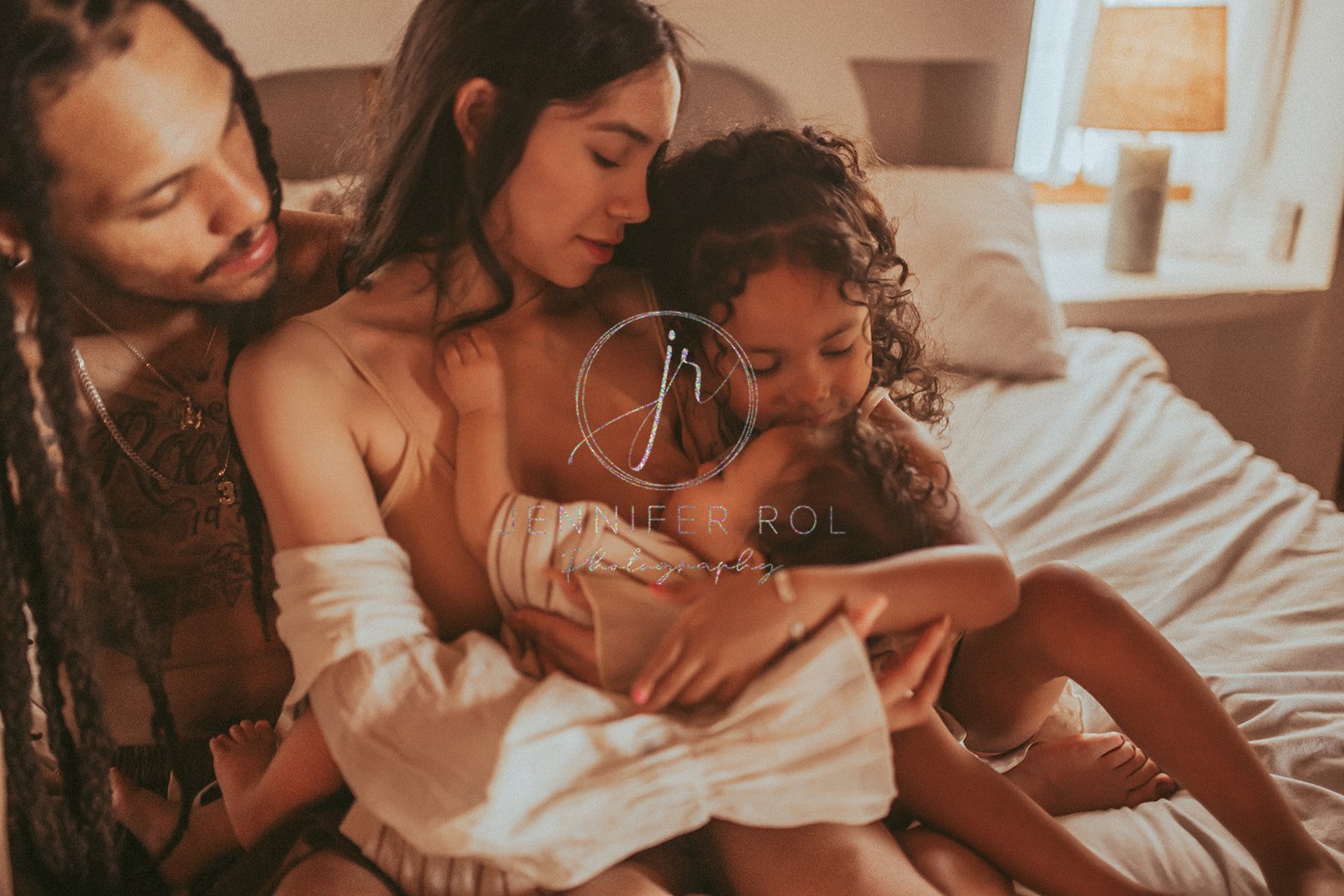 A mom breastfeeds her infant son with her husband and toddler daughter on a bed before some Missoula toddler activities