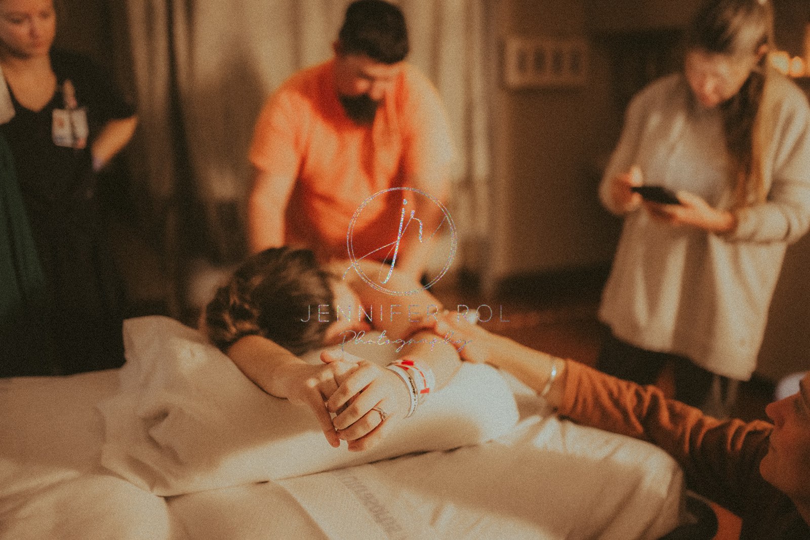 Details of a mom laying on a hospital bed with her birth team around her