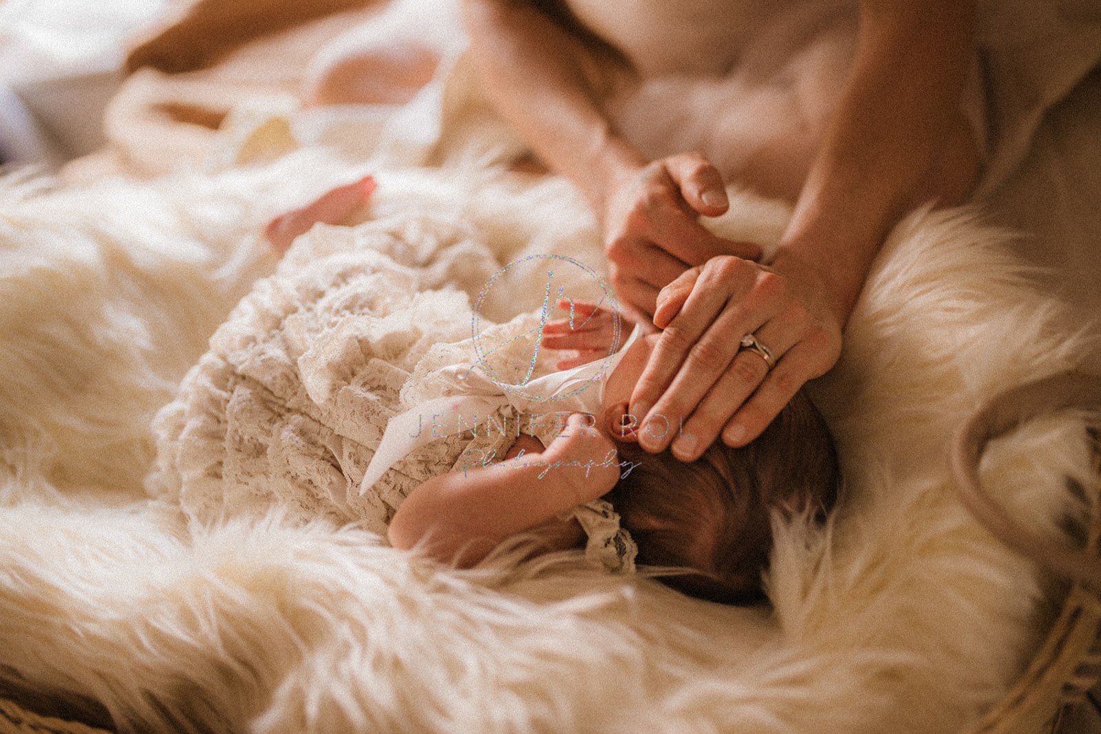 A mom rests her hand on her newborn daughter's head while laying in a fur blanket and lace dress after visiting Sistermoon Wellness