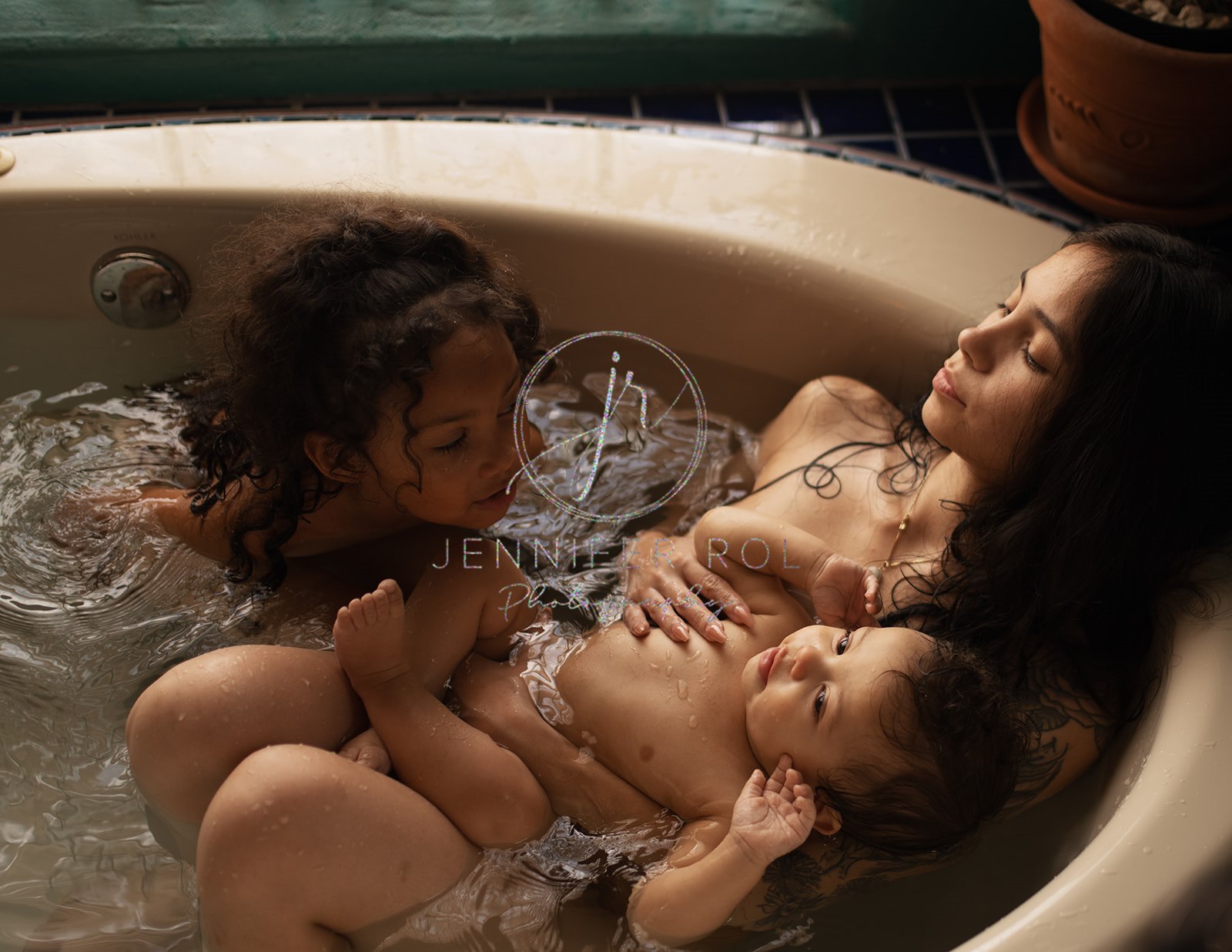 A mom lays in a tub taking a bath with her toddler daughter and baby son after using Jess4Sleep Consulting
