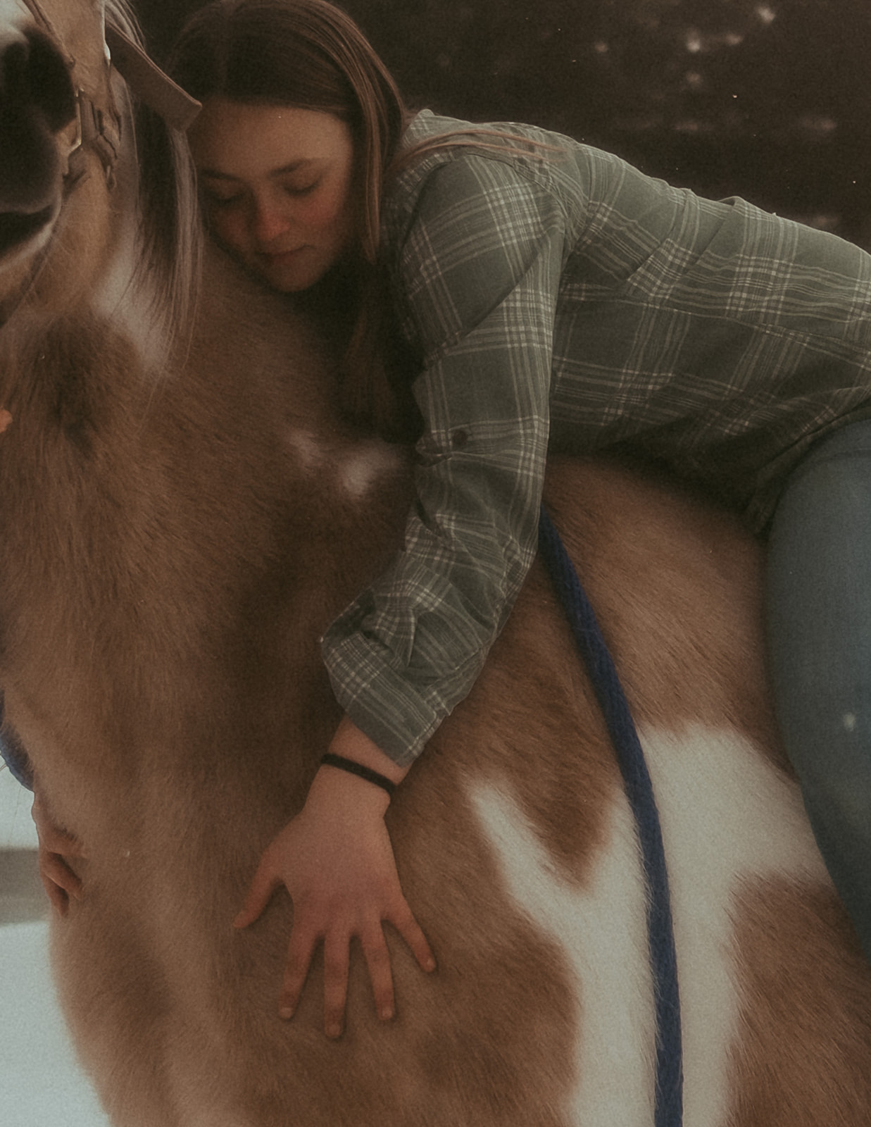 A woman lays on a horse and hugs its neck in a snowy pasture