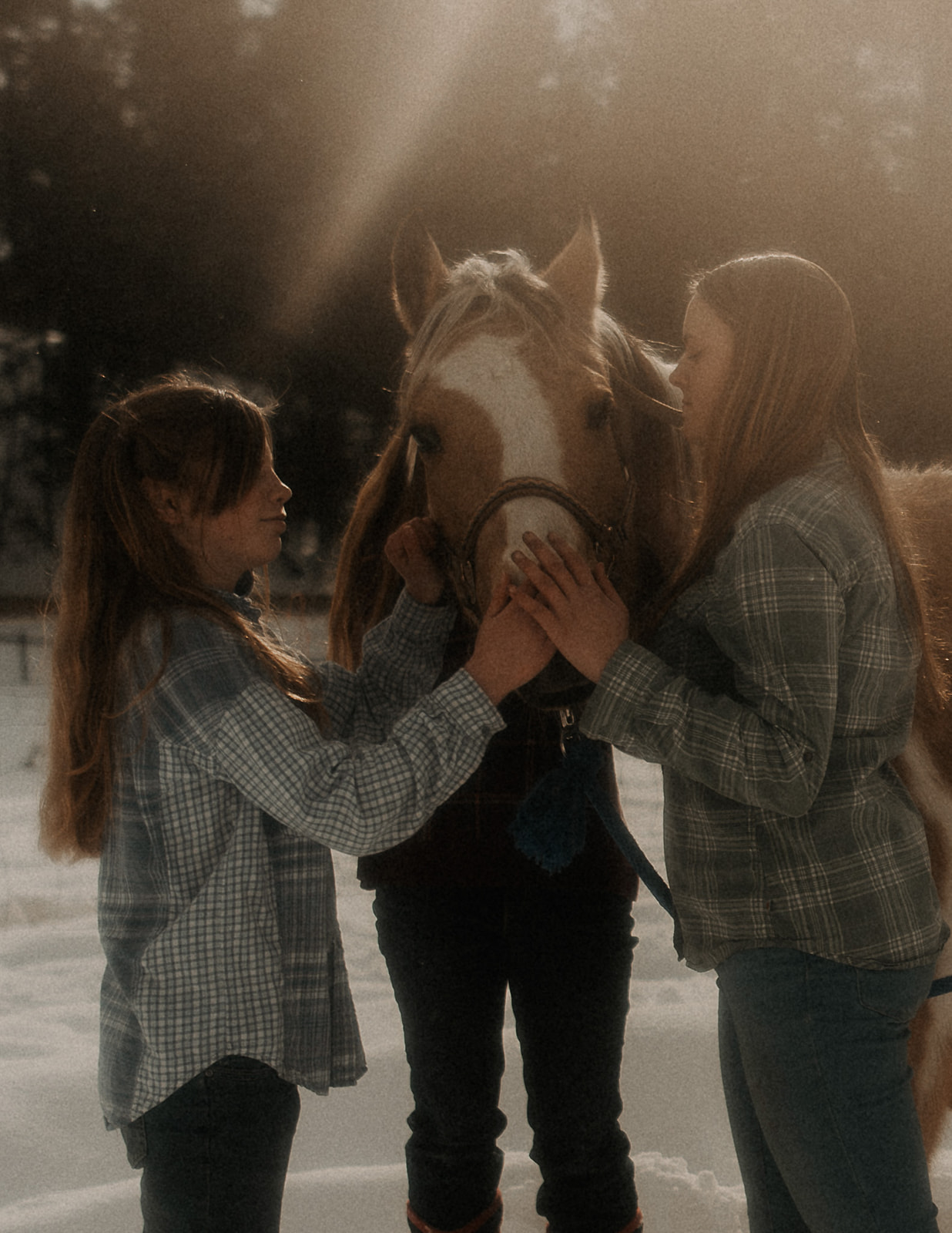 Two women hold the nose of a horse in a snow covered field at sunset after visiting EmPower Place