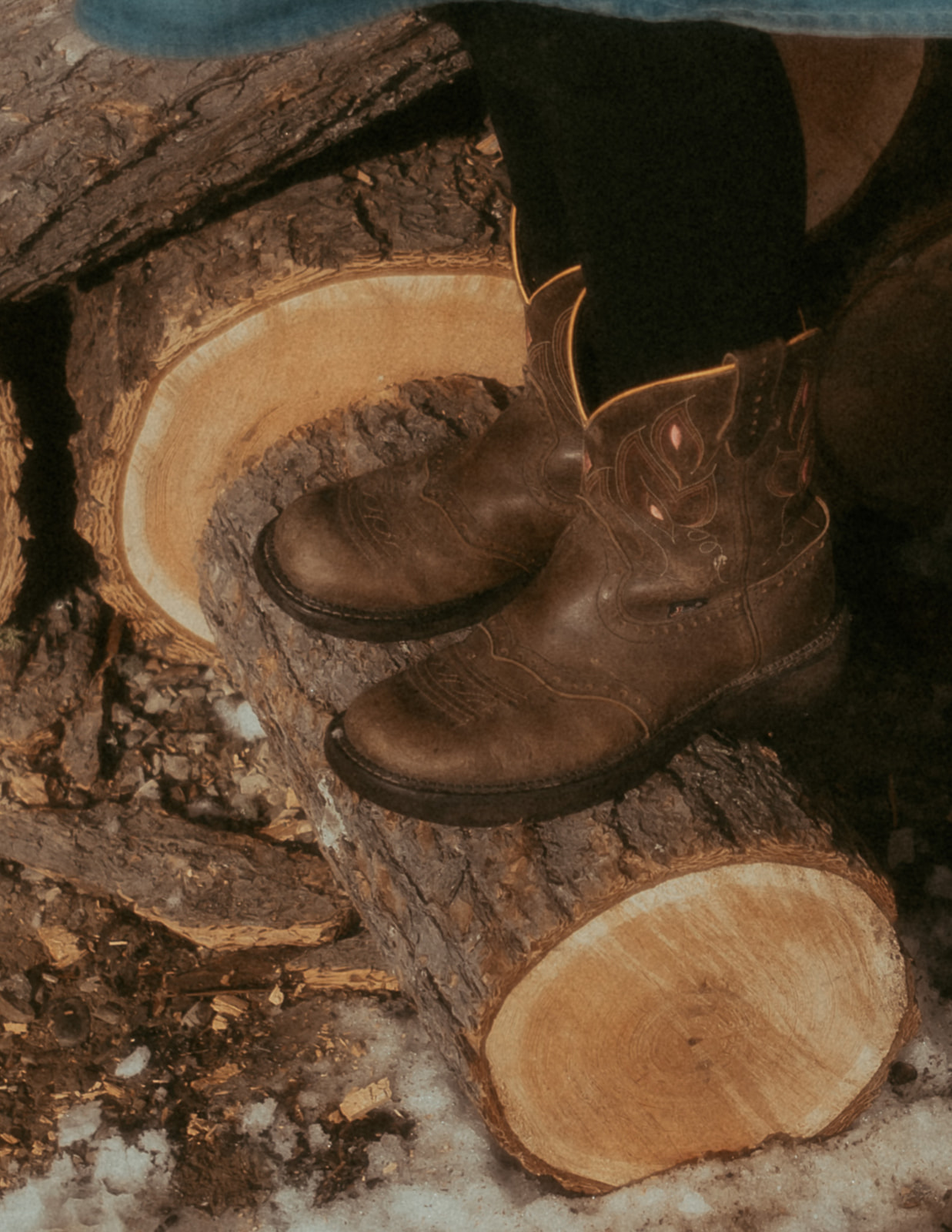 Details of a girl's boots on a cut log with black leggings