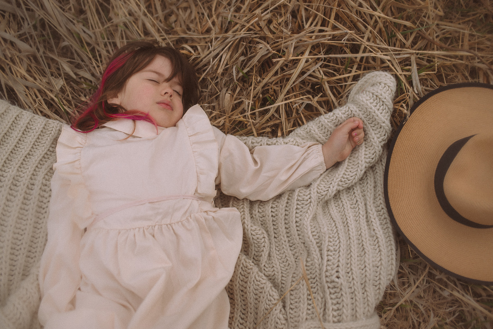 A young girl in a white dress sleeps on a knit blanket on hay after visiting Dragon Hollow Missoula
