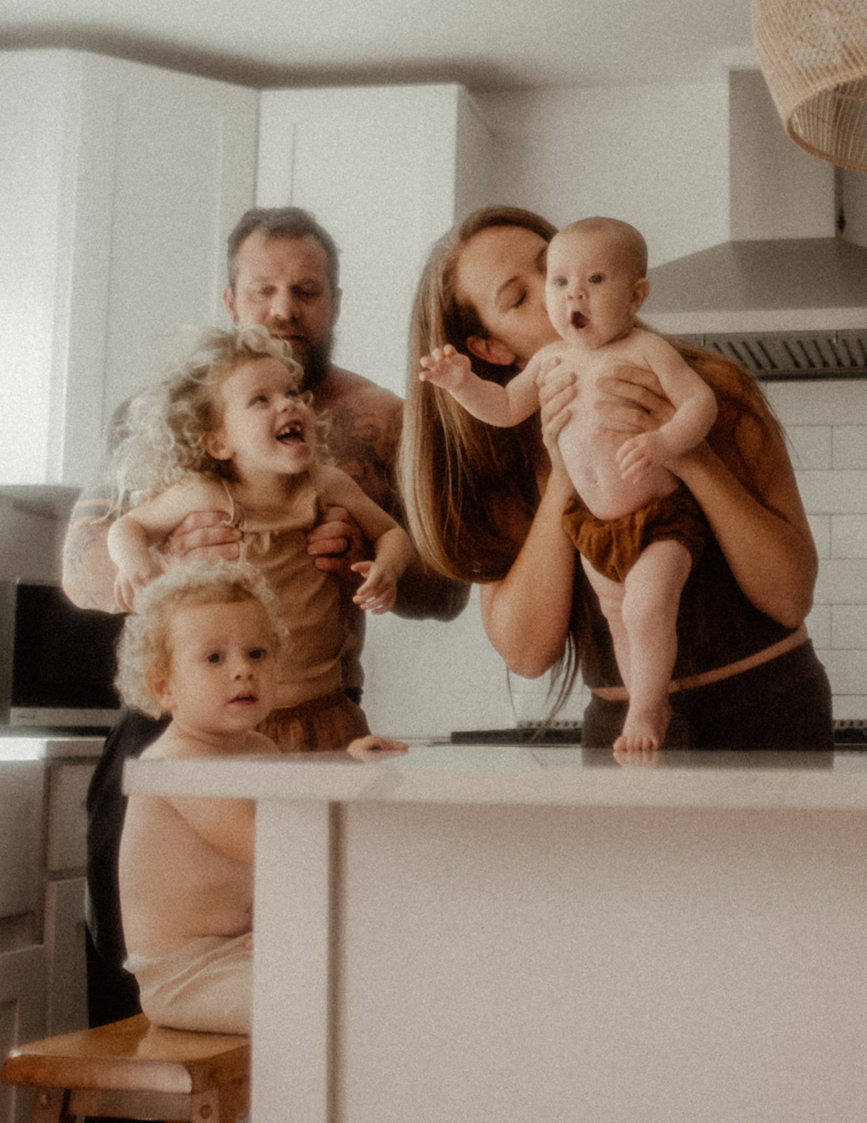 A baby and toddler laugh while playing with mom and dad in the kitchen