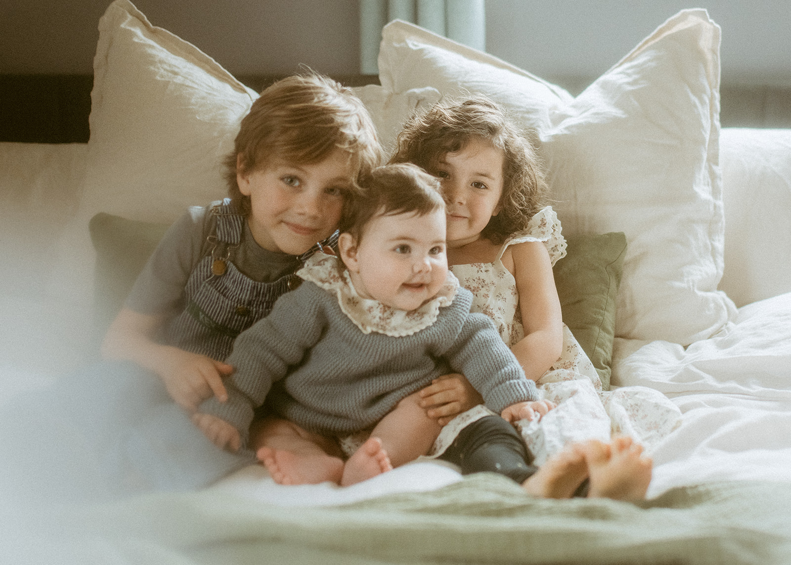 Three happy siblings hug and play on a bed with big smiles before visiting the Historical Museum At Fort Missoula