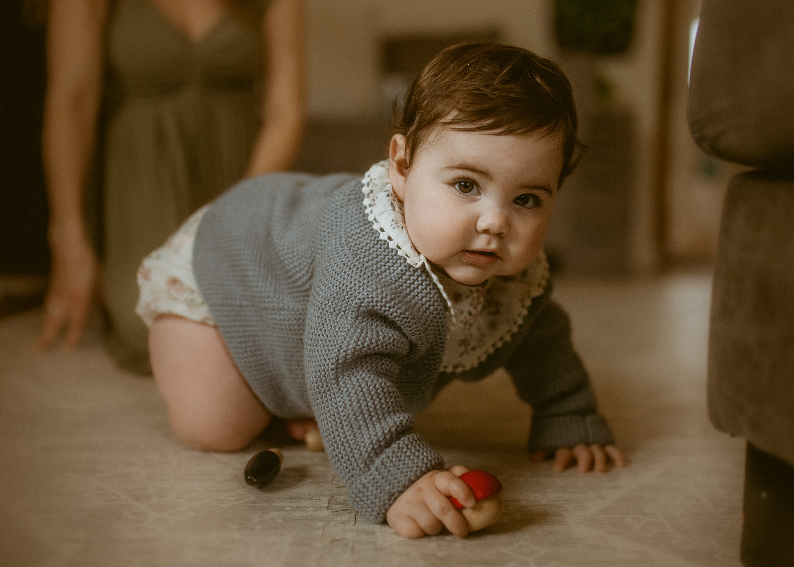 A baby girl in a knit sweater crawls across some matts in the living room before visiting the Historical Museum At Fort Missoula