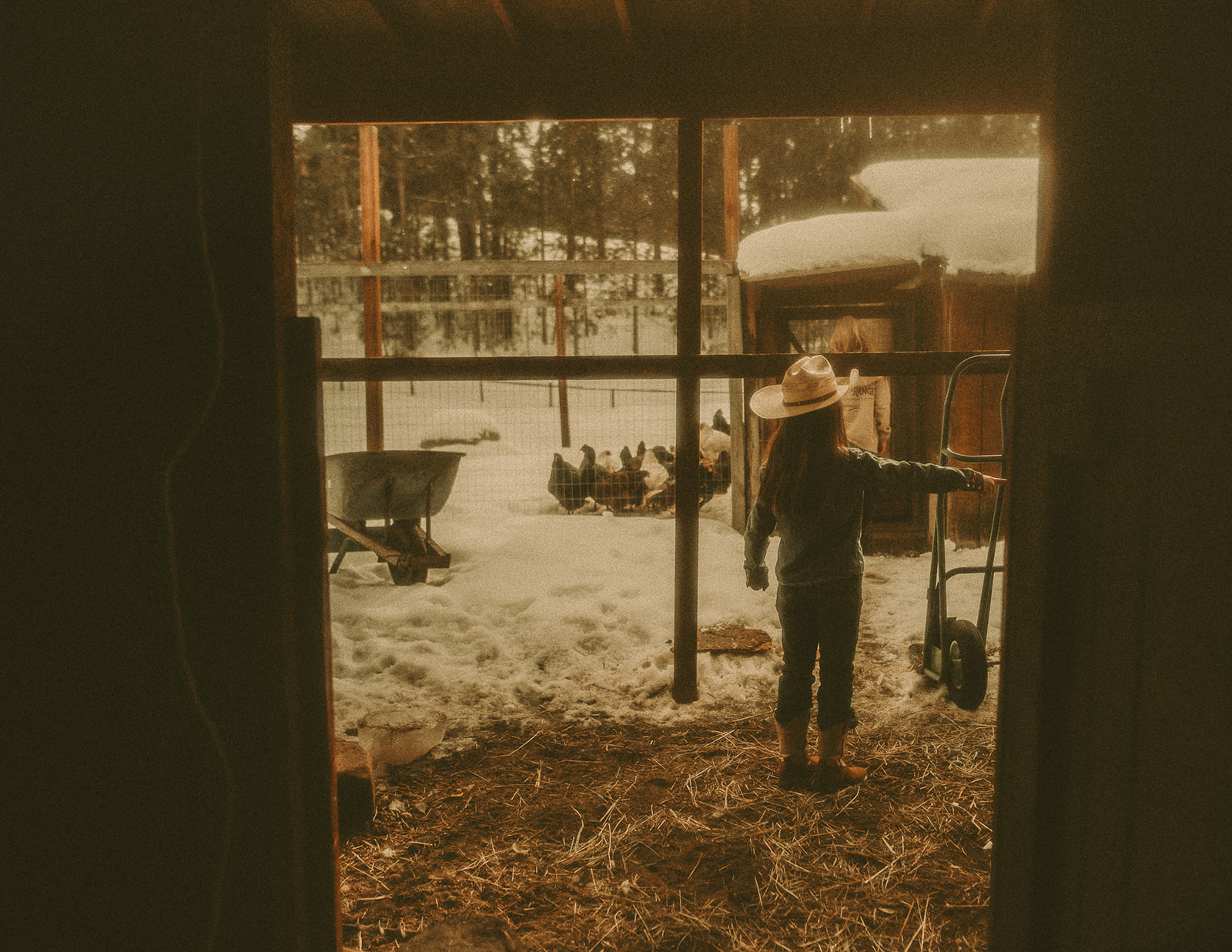 A young girl in a cowboy hat works in the barn in boots and denim on a snowy day before visiting the River City Roots Festival