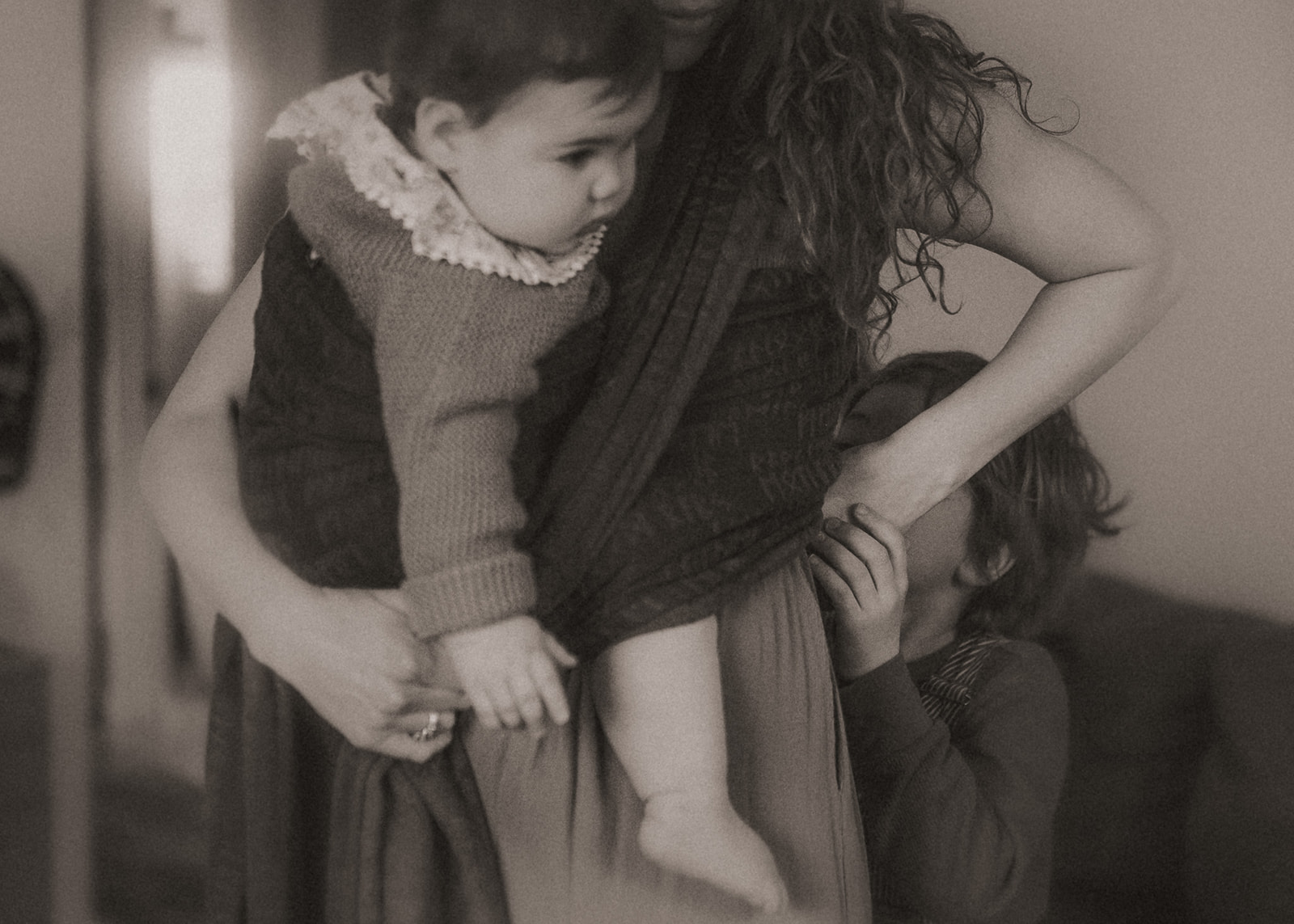 A young boy helps mom adjust her sling holding her infant against her chest