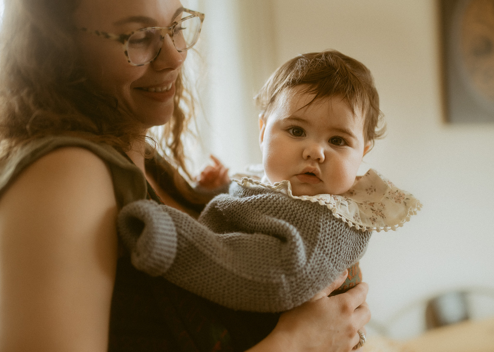 A happy mom holds her infant in a knit sweater in the kitchen before visiting the Clark Fork River Market