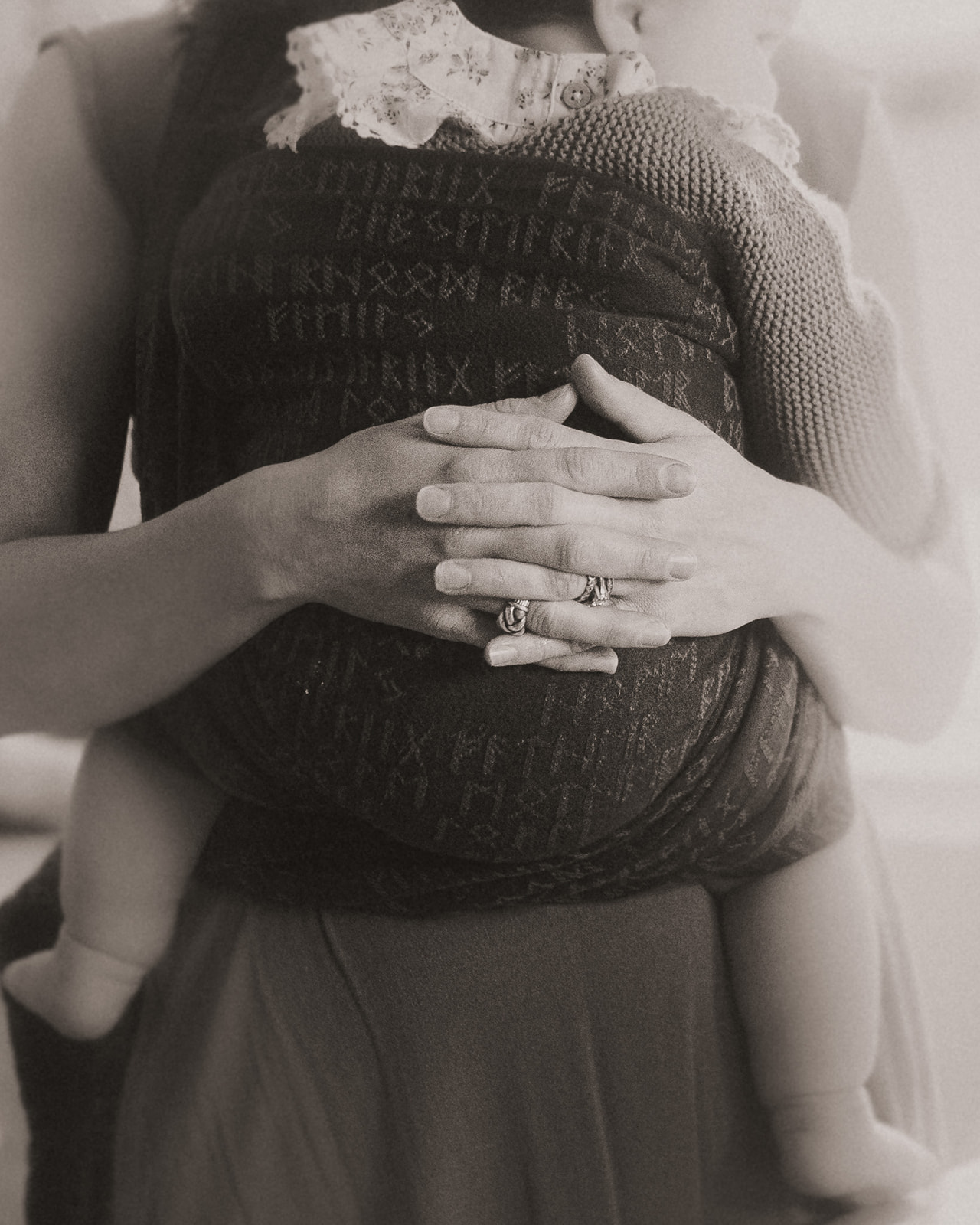 Details in black and white of a mom holding her infant against her chest wrapped in a carrier before visiting Clark Fork River Market