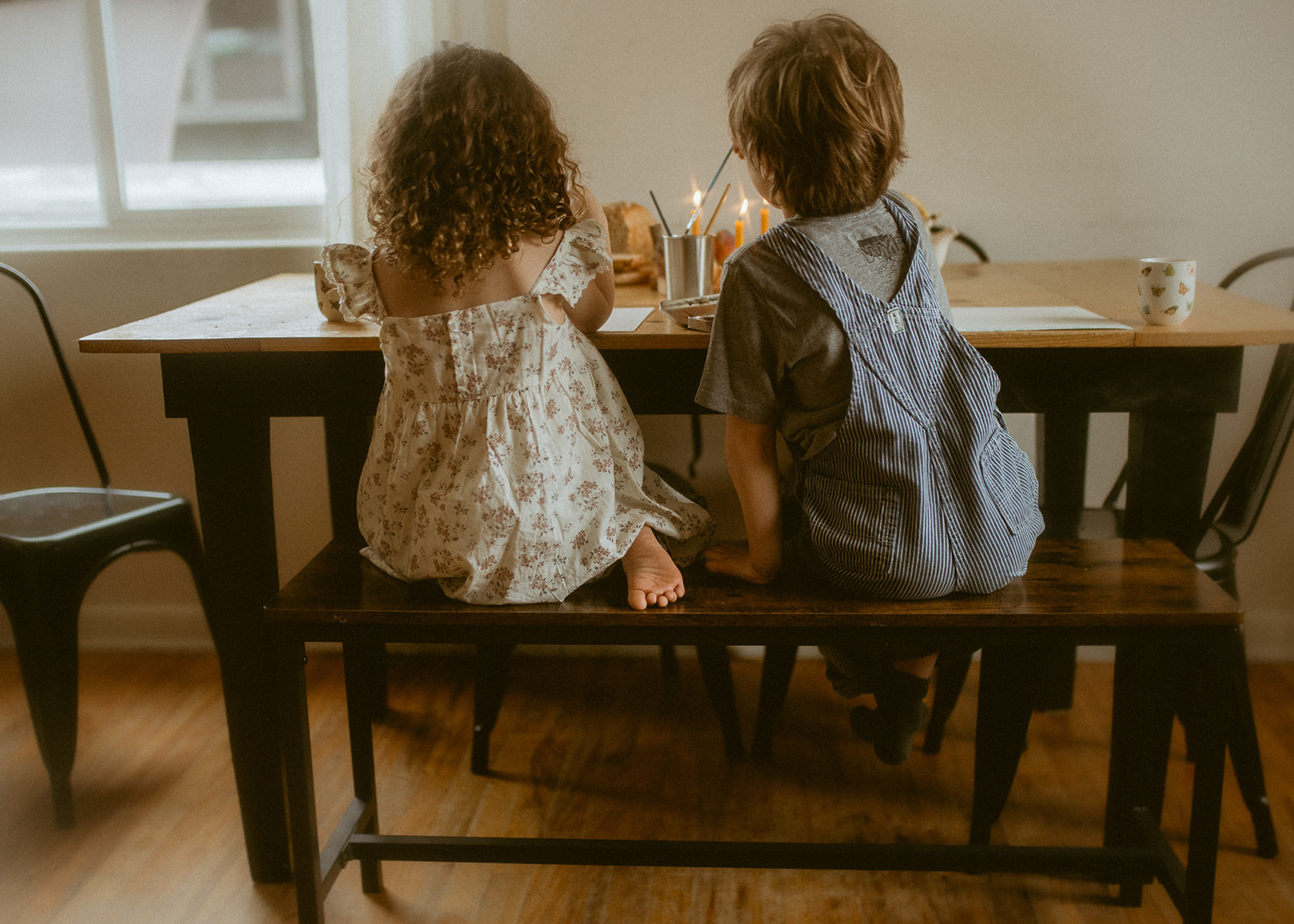 Toddler brother and sister in a dress and overalls paint together at the dining room table after visiting Discovery Preschool Missoula