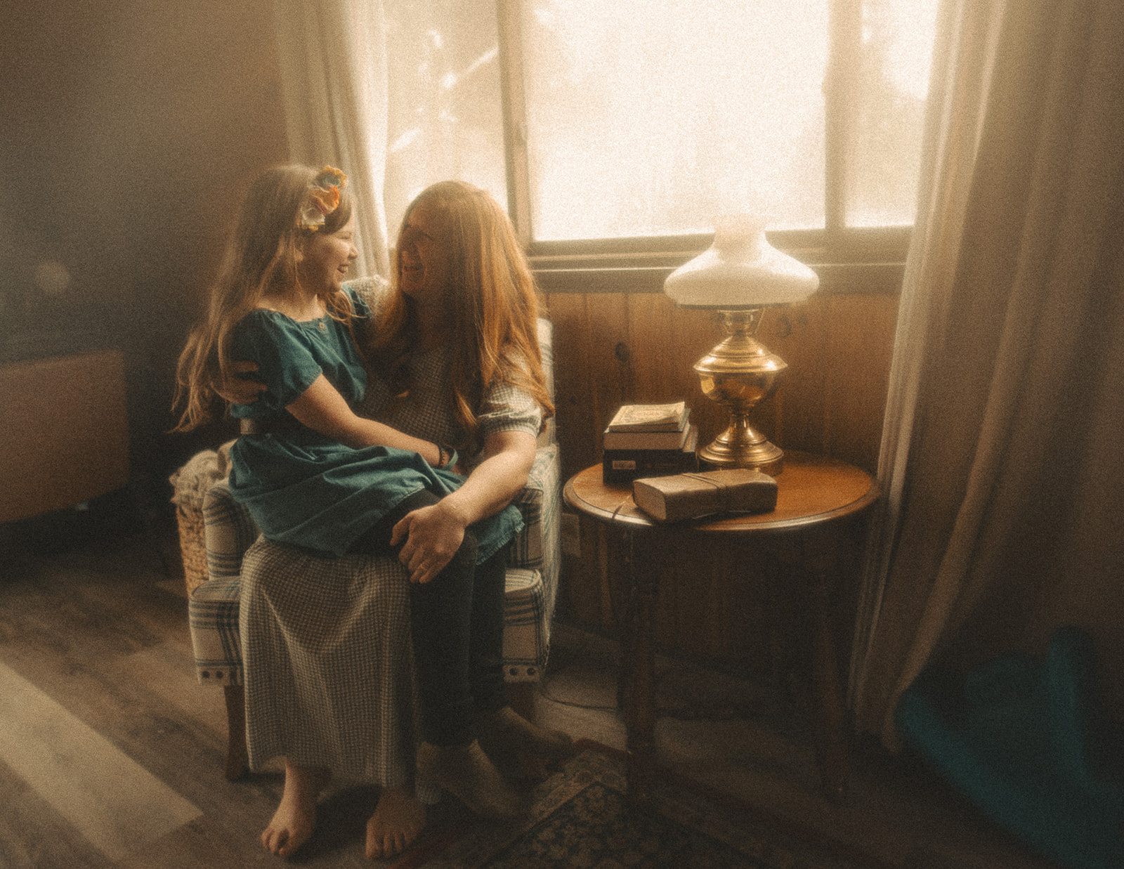 A happy mom sits in the living room with her young daughter in her lap as they both laugh