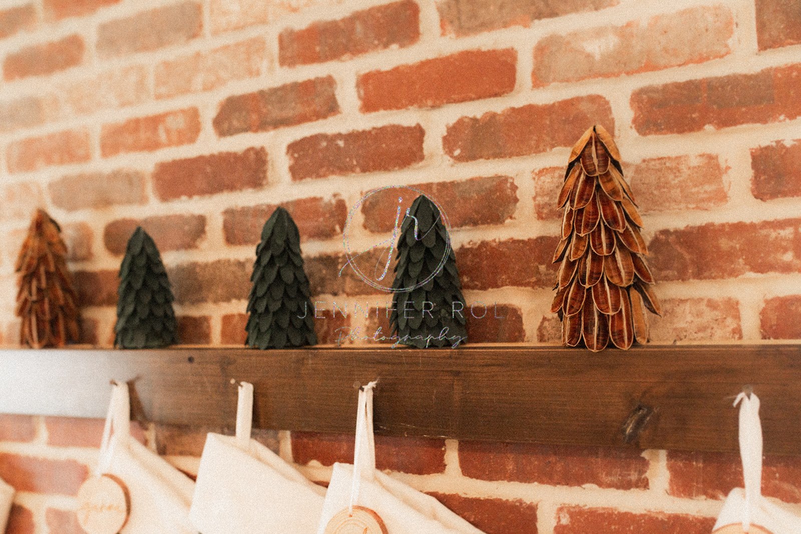 Details of wooden christmas trees on a mantle on a brick wall above stockings