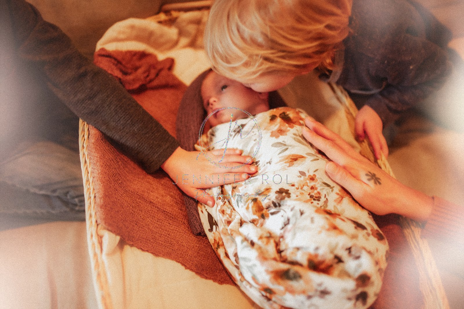 A blonde toddler in a blue sweater leans in to kiss his newborn baby sister in a crib before visiting Missoula, MT festivals