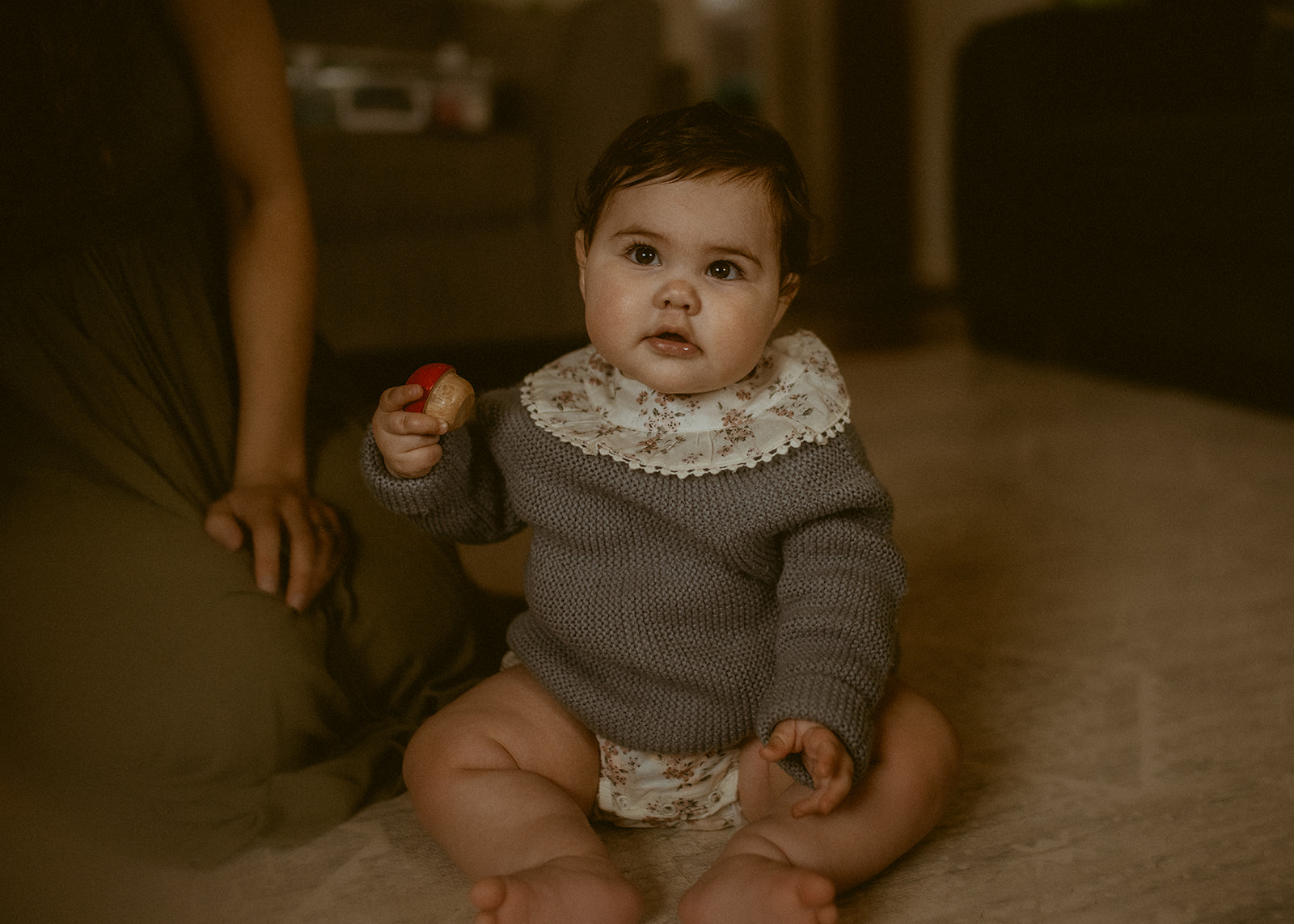 A baby sits on the living room floor playing with a wooden toy before heading to Out To Lunch Missoula