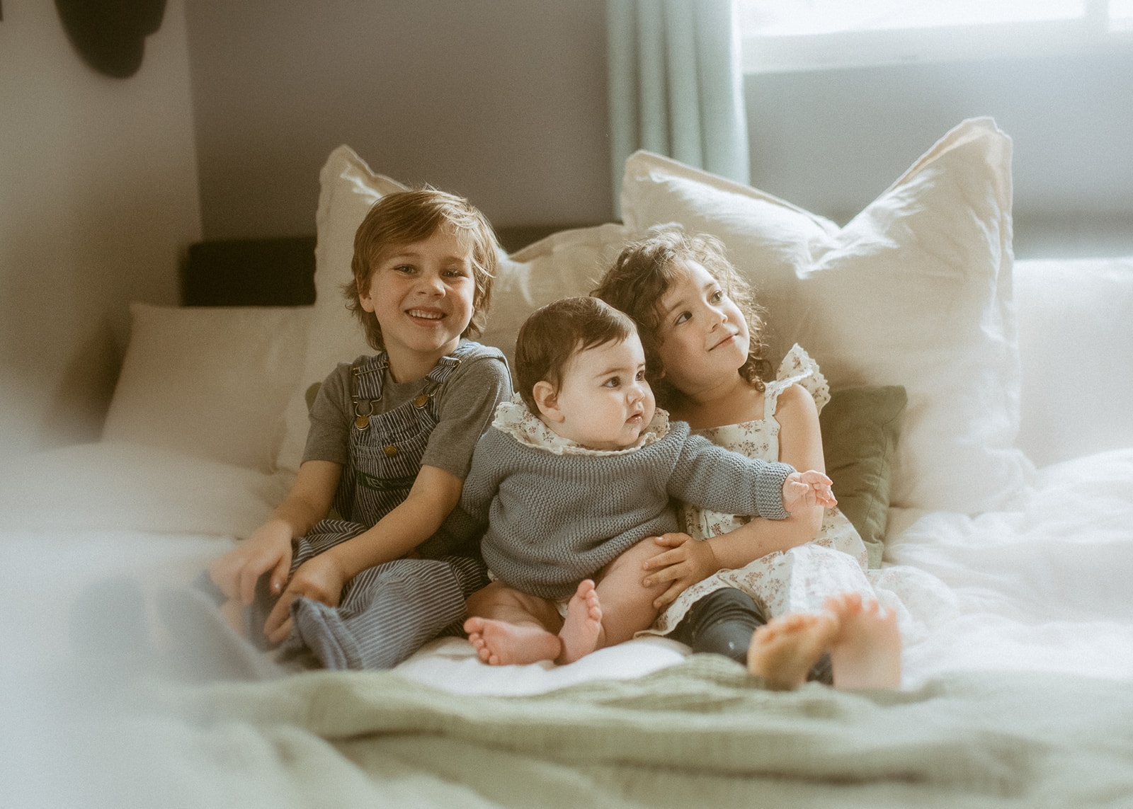 A happy brother and sister smile on a bed with their infant baby sister between them before some rafting in Missoula
