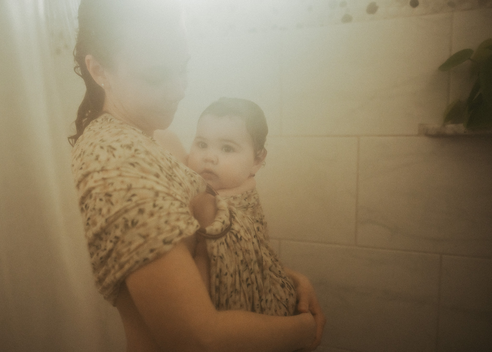 A mother showers with her infant in a sling on her chest
