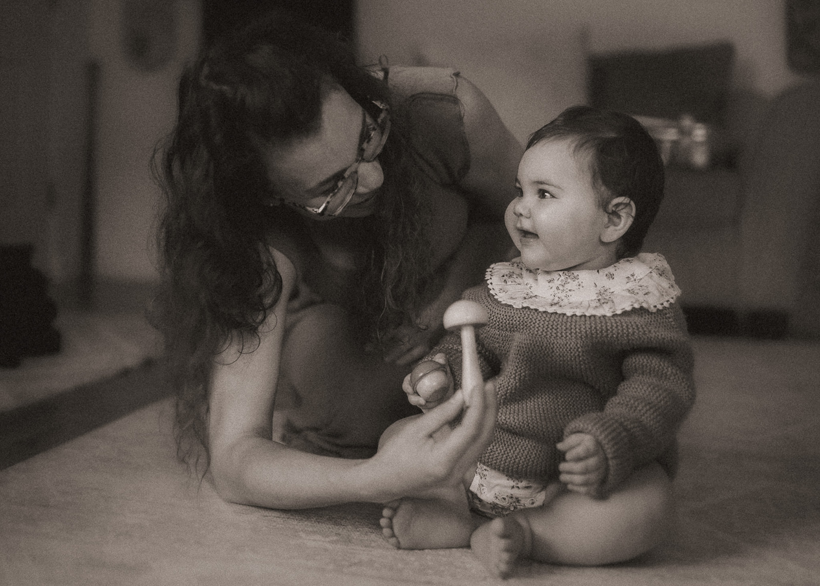 A mom plays with wooden mushrooms with her smiling baby in a knit sweater in a living room before tubing in Missoula