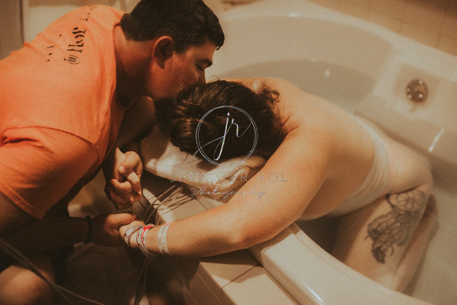 A husband holds the hand of and kisses his wife in labor as she kneels in a tub at a birthing center in Hamilton, MT