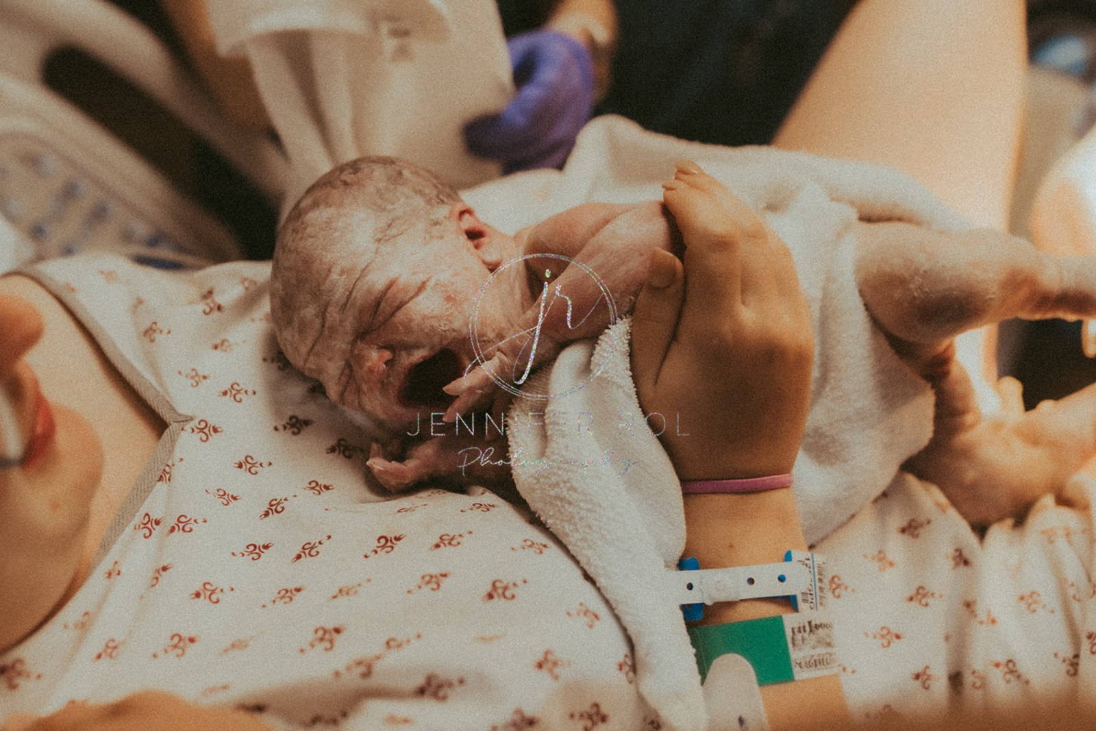 A screaming newborn baby lays on mom's chest wrapped in blankets at a birthing center in Hamilton, MT