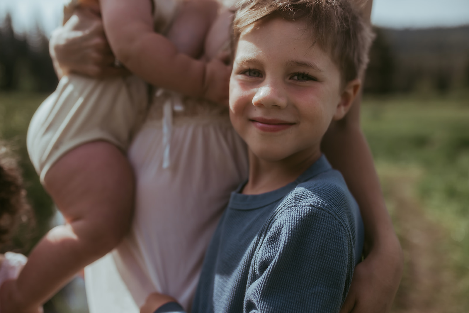 A smiling toddler boy in a blue shirt hugs on mom in a field after visiting Ignite Creative School