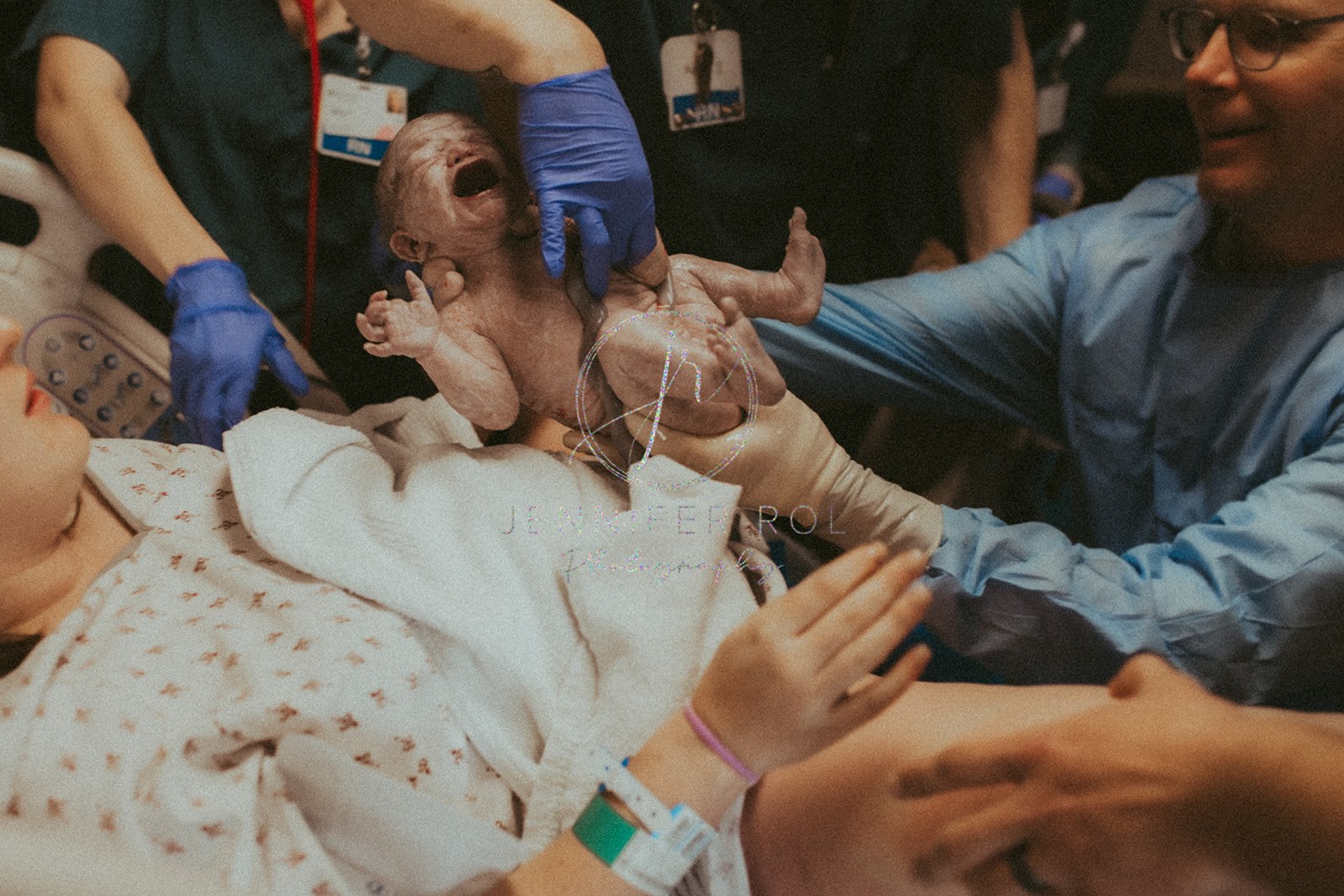 A fresh newborn baby is handed to mom by medical staff in a hospital bed