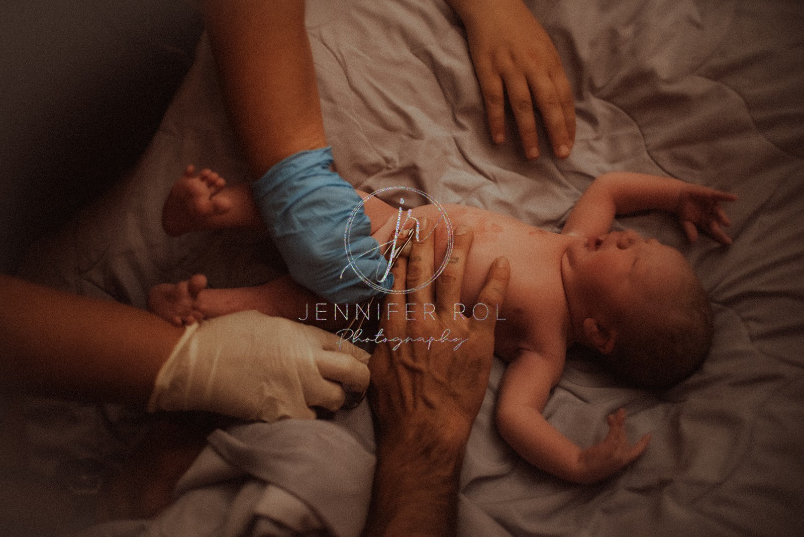 A midwife in Hamilton, MT cuts the umbilical cord on a newborn on a bed with mom and dad's hands