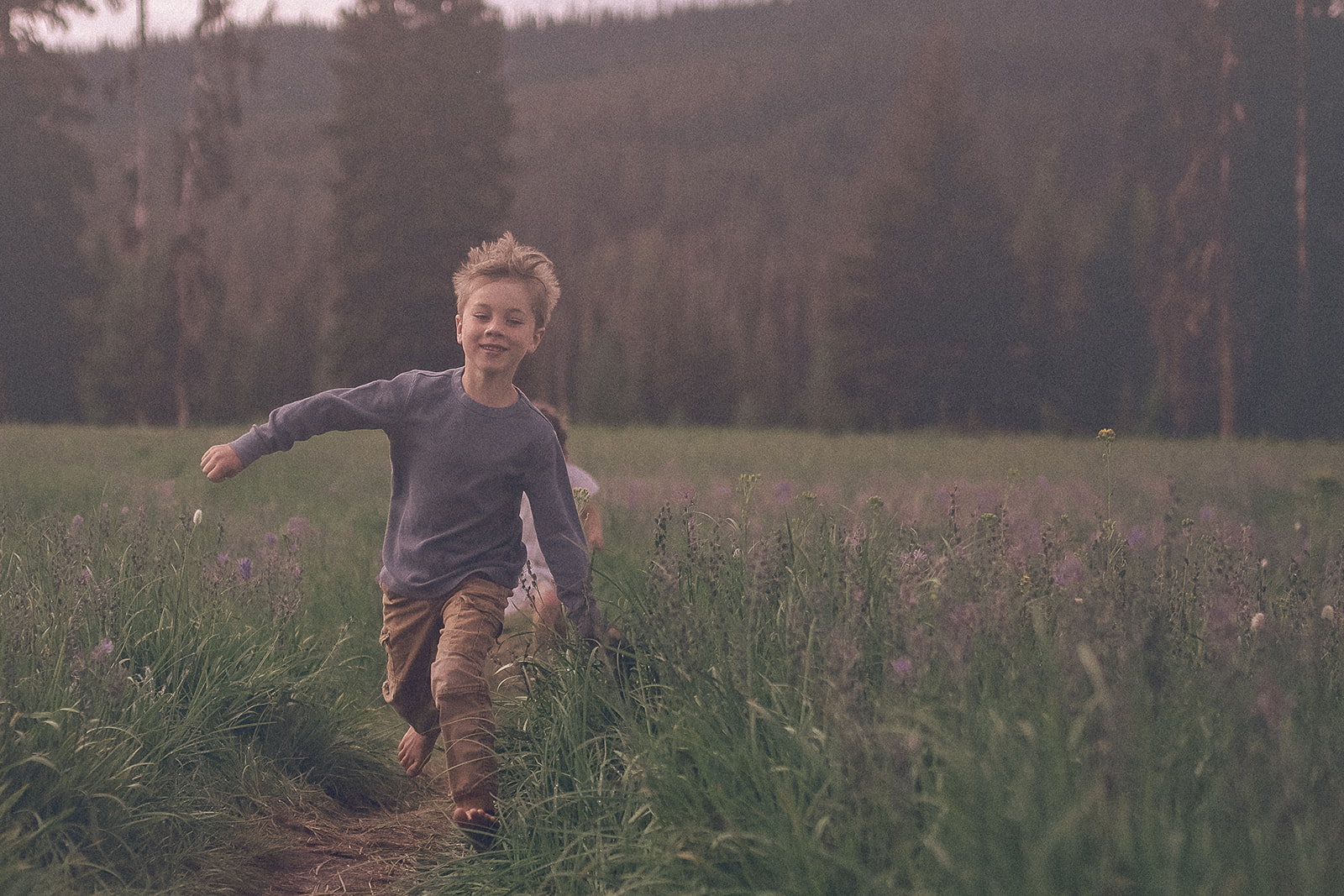 A young boy runs up a pasture trail through wildflowers in a blue shirt and khaki pants after attending Missoula Homeschool Co-Op events