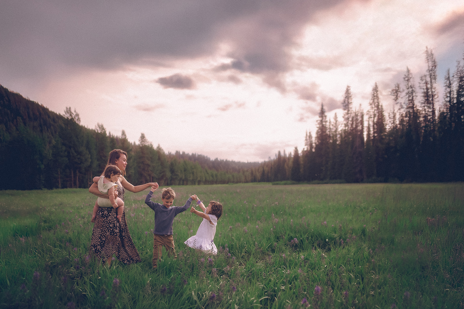 A happy mom dances with her three young children in an open blooming pasture after joining Missoula Homeschool Co-Op
