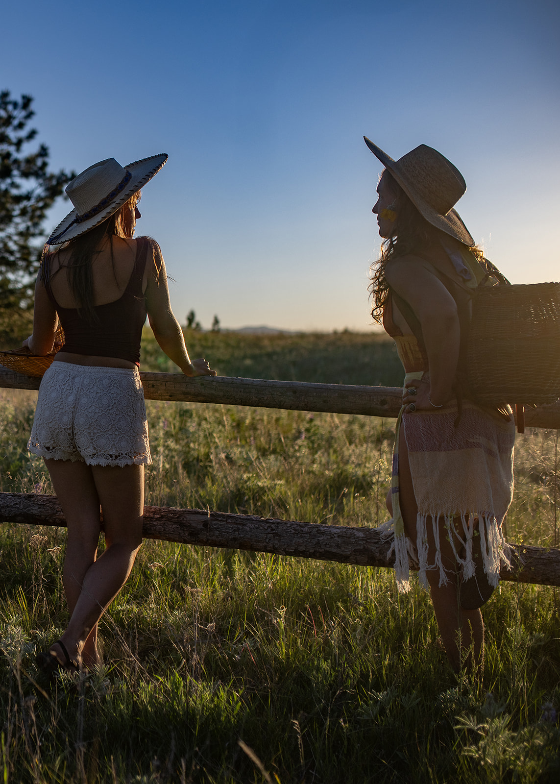 Two women in big hats lean on a pasture fence at sunset after meeting with Somatic Connections
