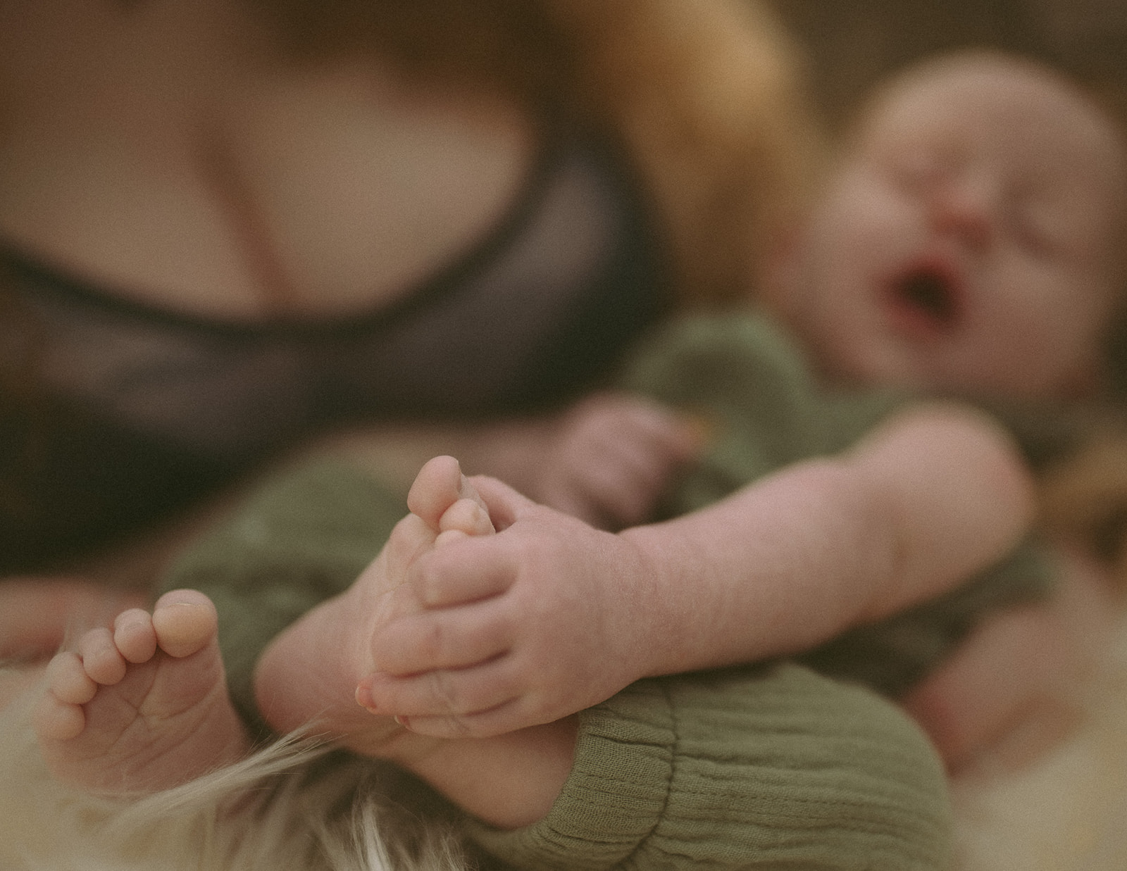 Details of a newborn baby's hand holding a foot in a green onesie