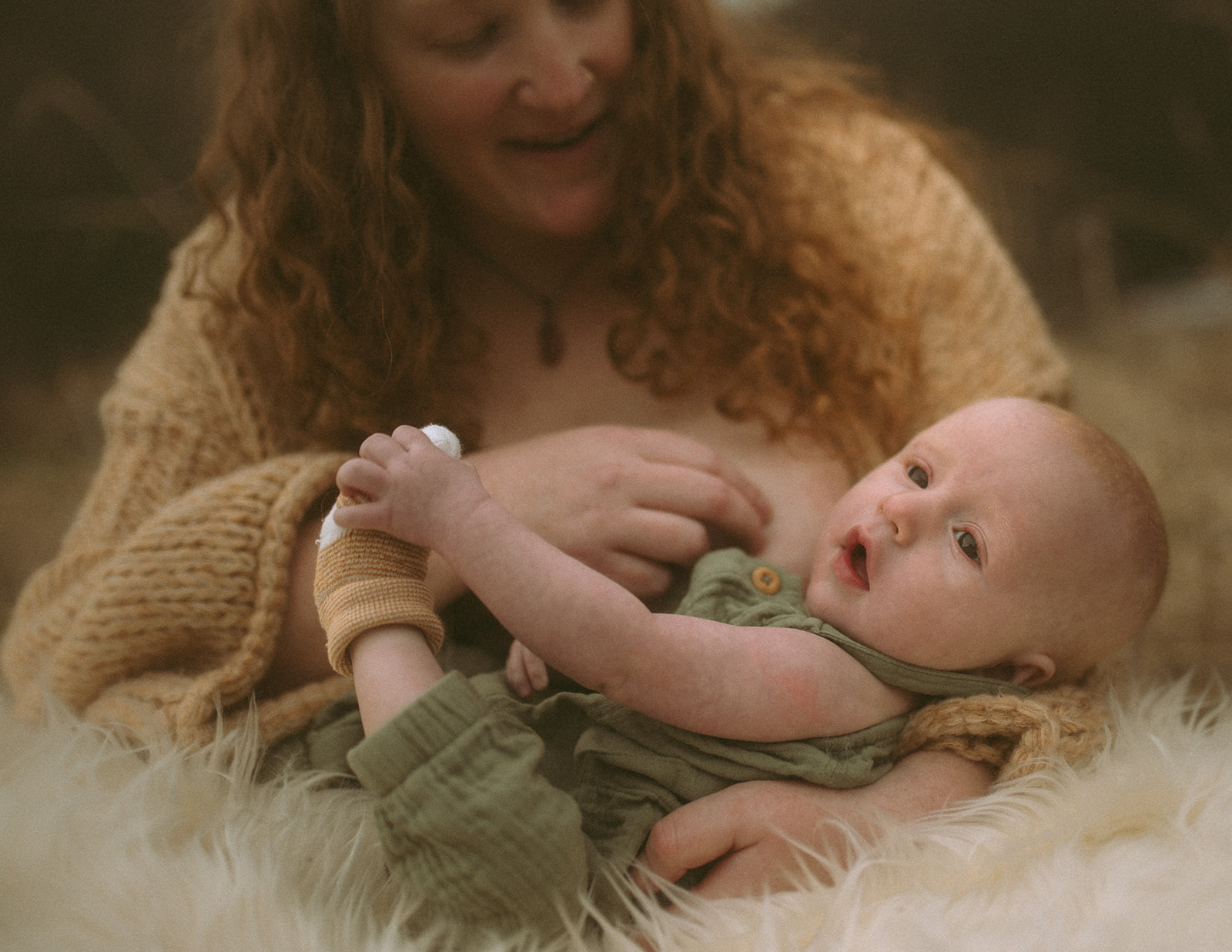 A baby in a green onesie lays in mom's arms as she prepares for breastfeeding thanks to Tierra Madre Midwifery