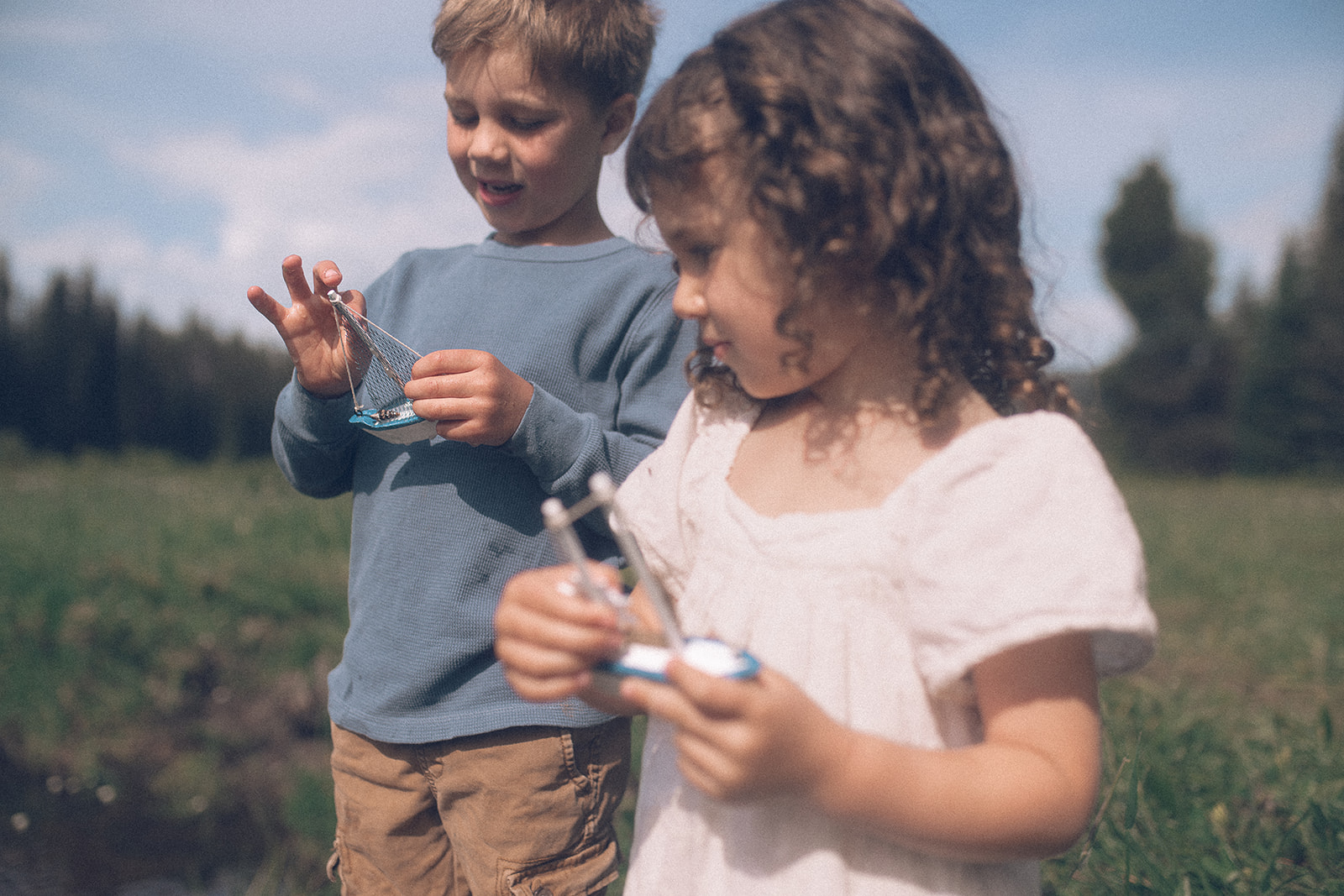toddler brother and sister play with toy boats by a creek after visiting this toy store in Hamilton, MT