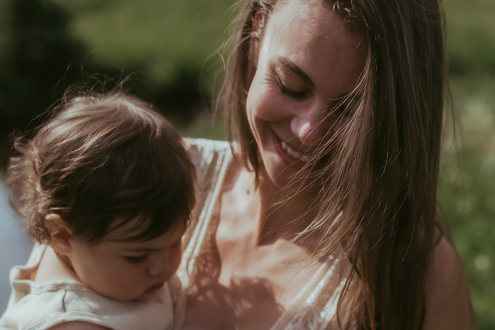 A smiling mother plays with her infant in her arms in a field after visiting Happy Kid Store