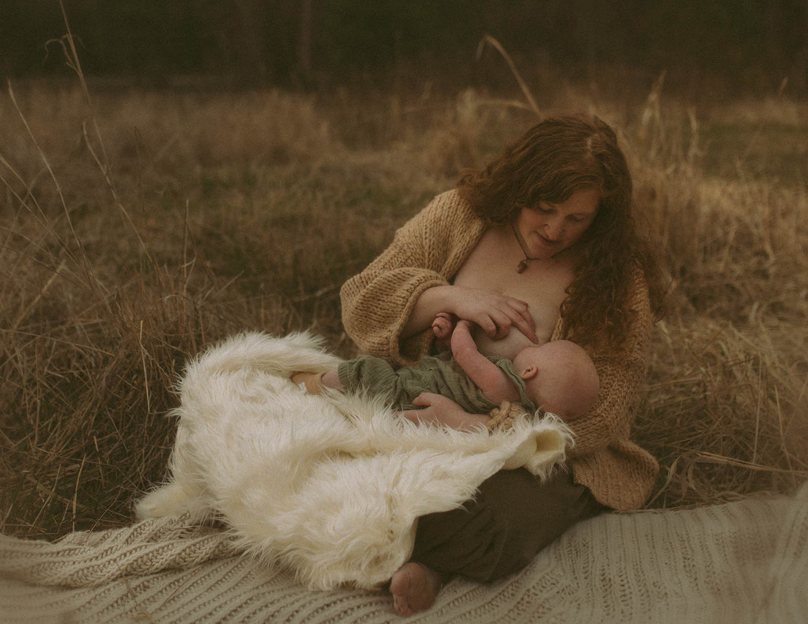 A new mother sits on a blanket breastfeeding her infant on a fur blanket in a golden pasture after finding pediatric dentists in Hamilton, MT